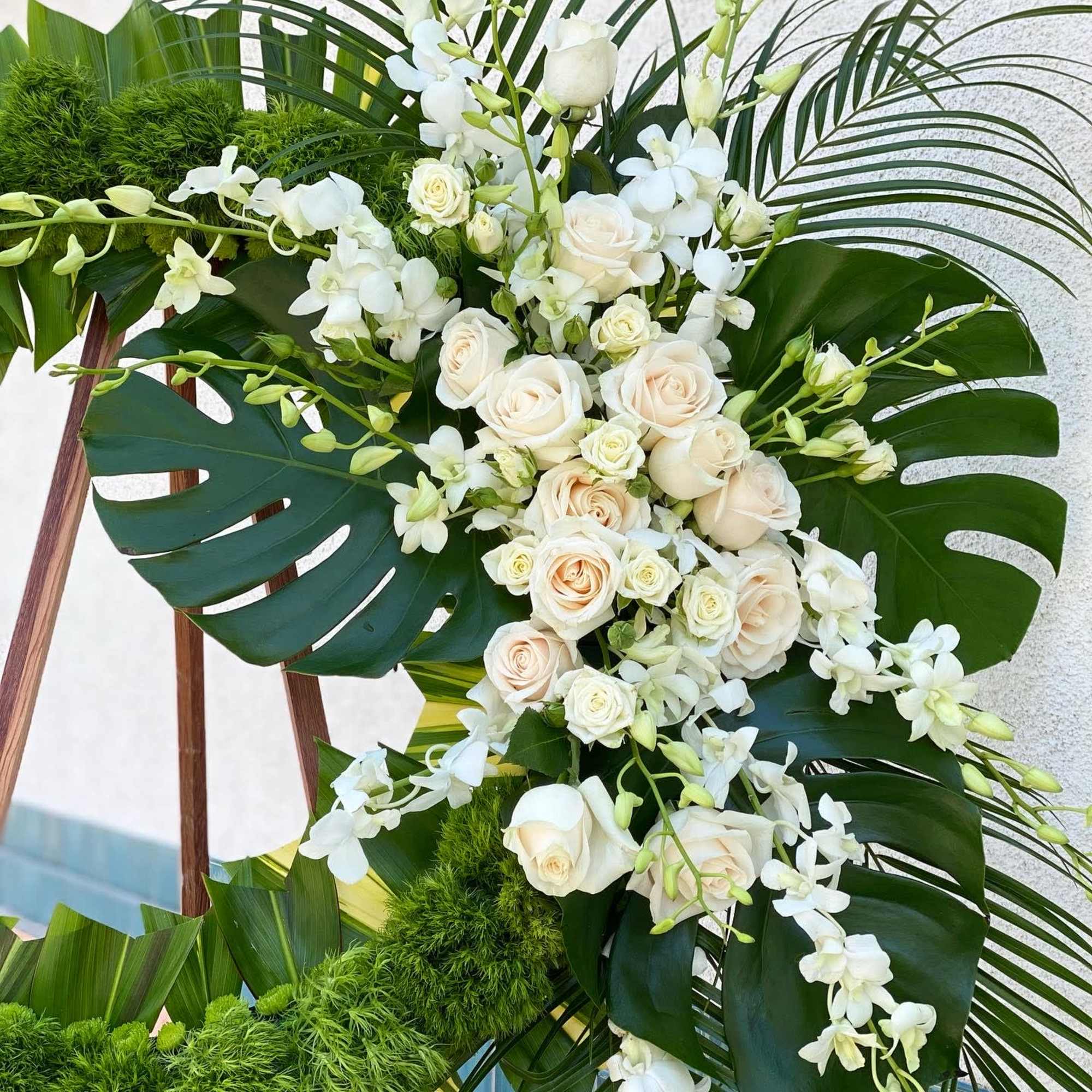 White roses and orchids arranged with large tropical leaves