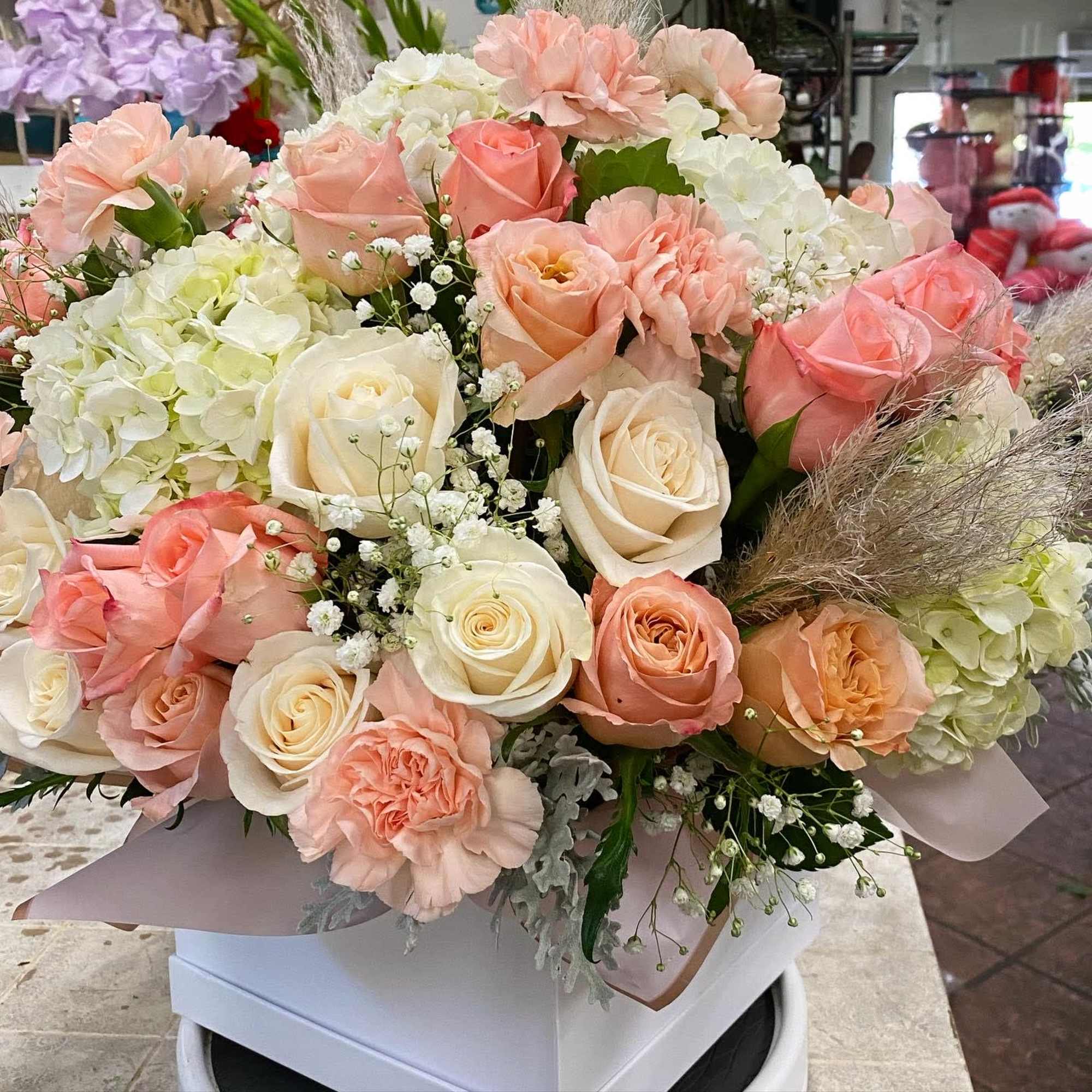 Bouquet of peach and white roses with pale hydrangeas in a box