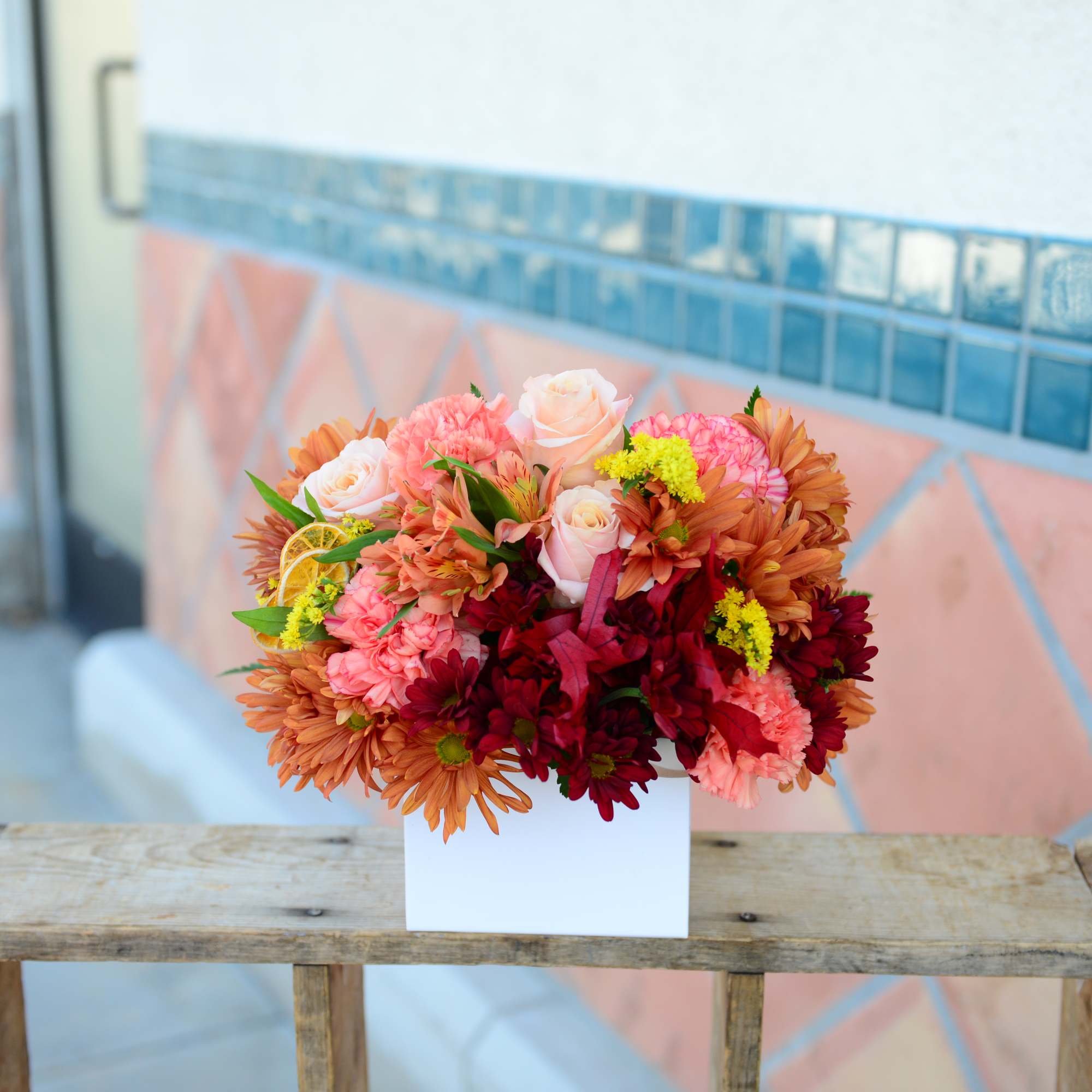 Mixed bouquet of pink, peach, and burgundy flowers in a white box