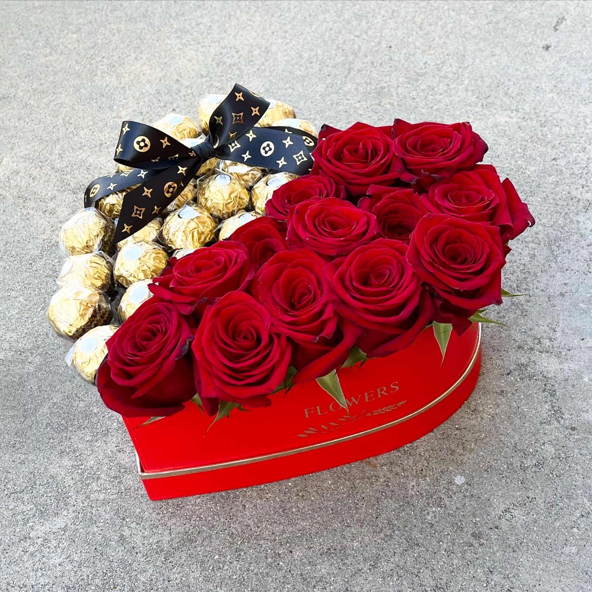Heart-shaped box with red roses and gold-wrapped chocolates tied with a black ribbon