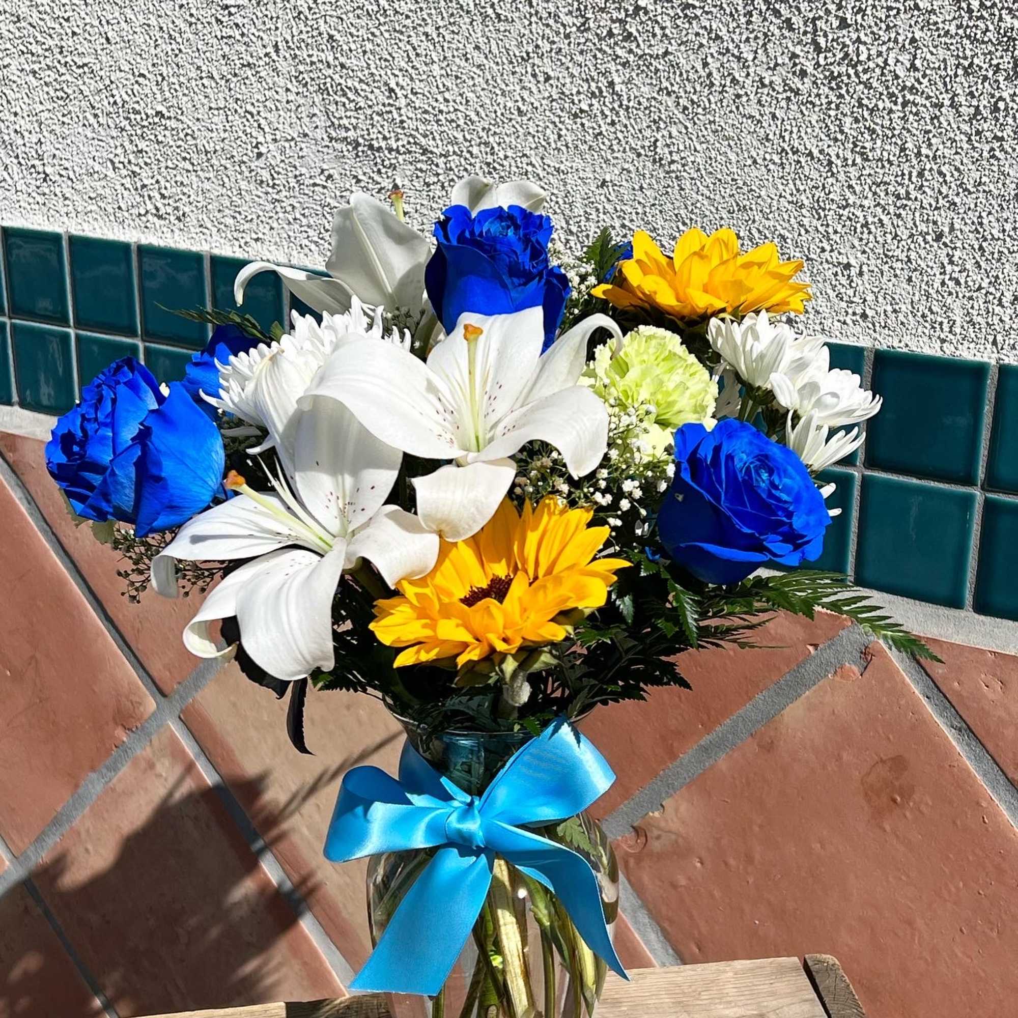 Bouquet of blue roses, white lilies, and yellow daisies in a glass vase with a blue ribbon