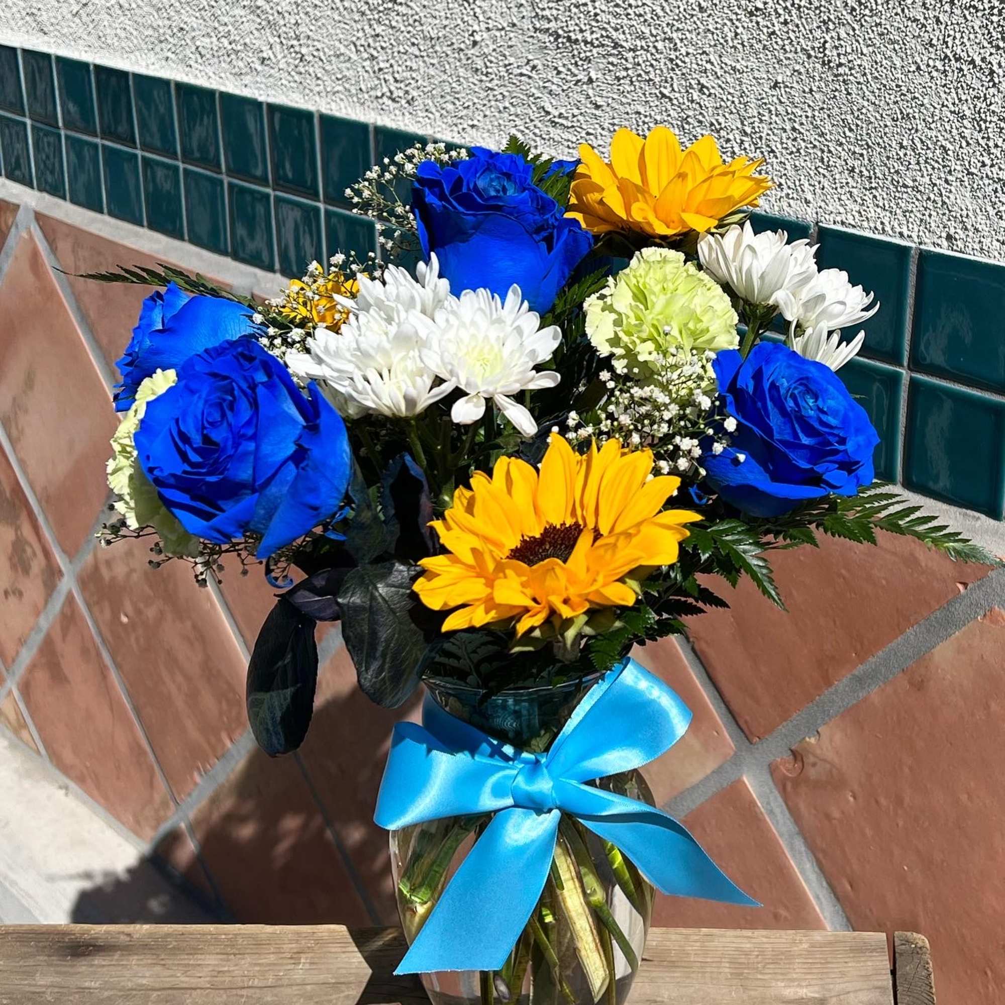 Bouquet of blue roses, yellow daisies, and white chrysanthemums in a glass vase