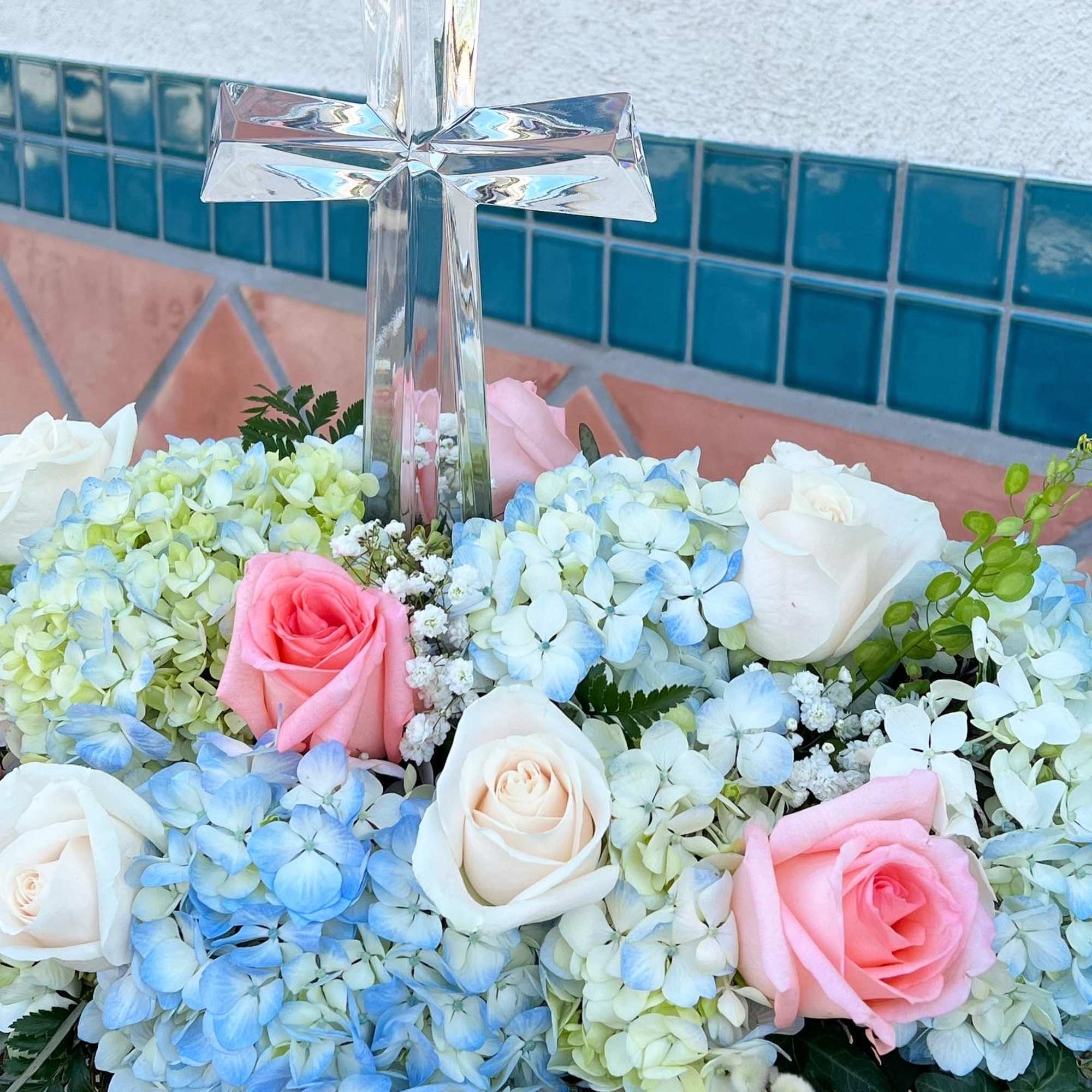 blue hydrangea and pastel roses are beautifully arranged with a crystal cross