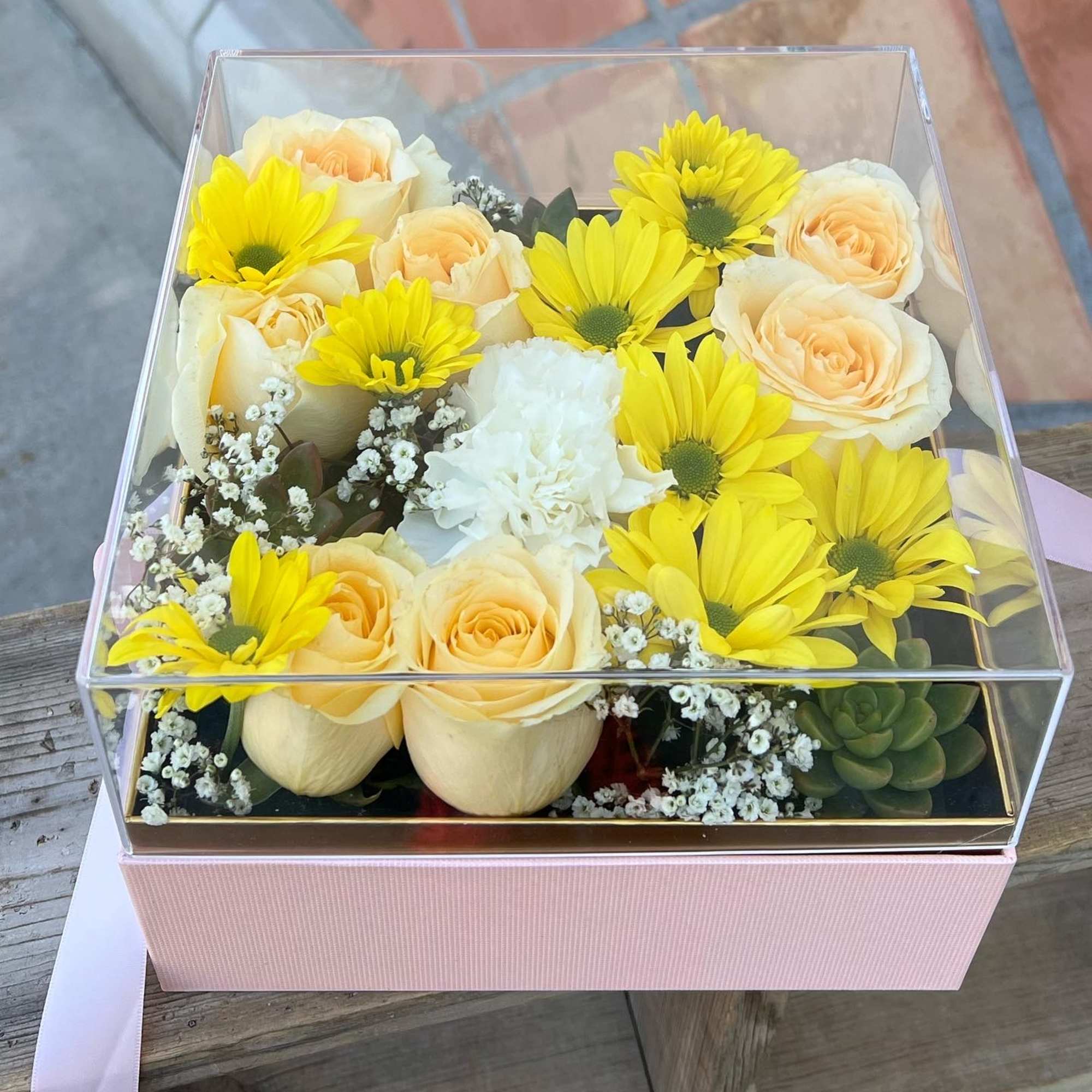 Yellow daisies and pale peach roses in a clear square box