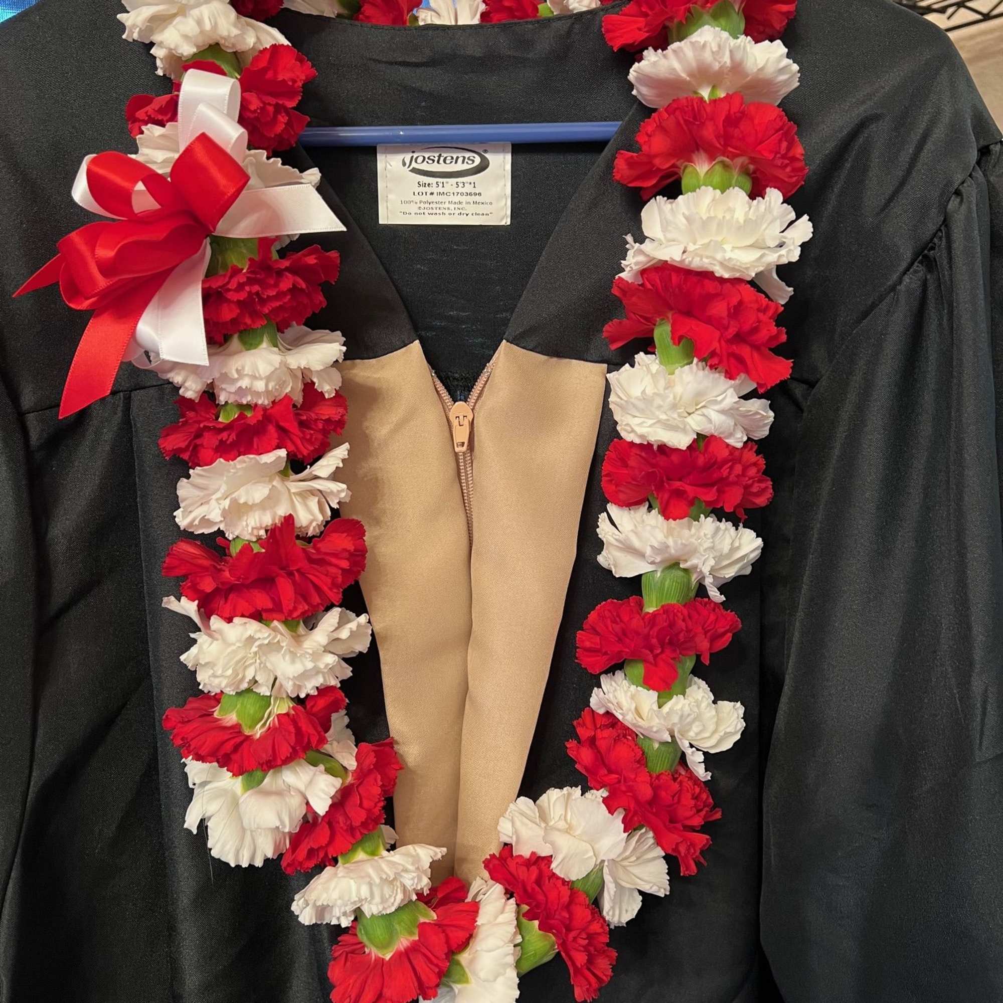 Red and white carnation lei draped over a black graduation gown