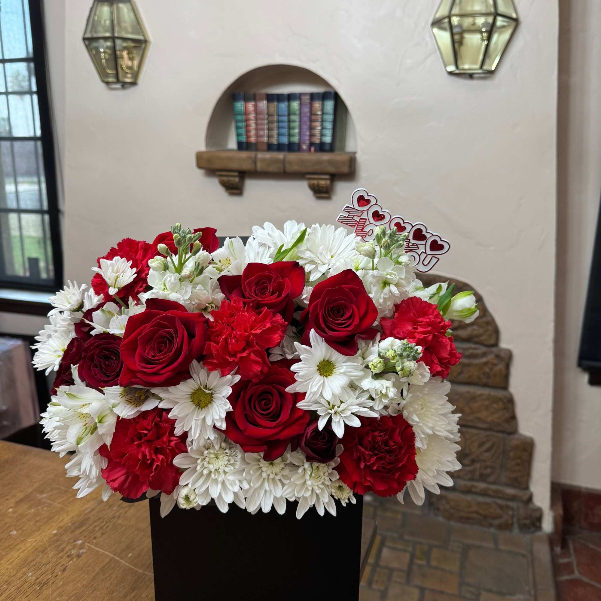 Red roses and white daisies arranged in a black box with a heart topper
