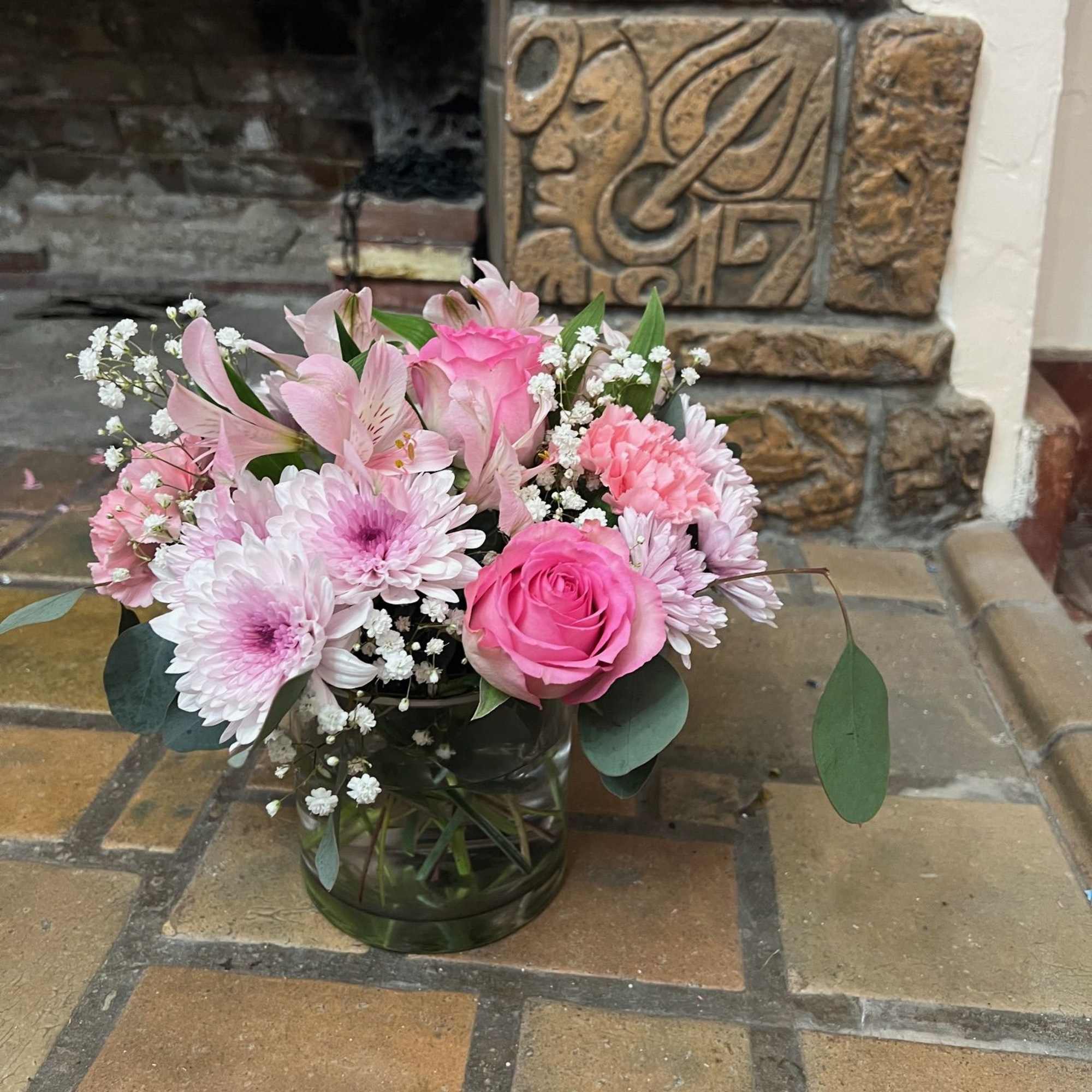 Different shade of pink flowers are arranged inside a clear cylinder vase.



