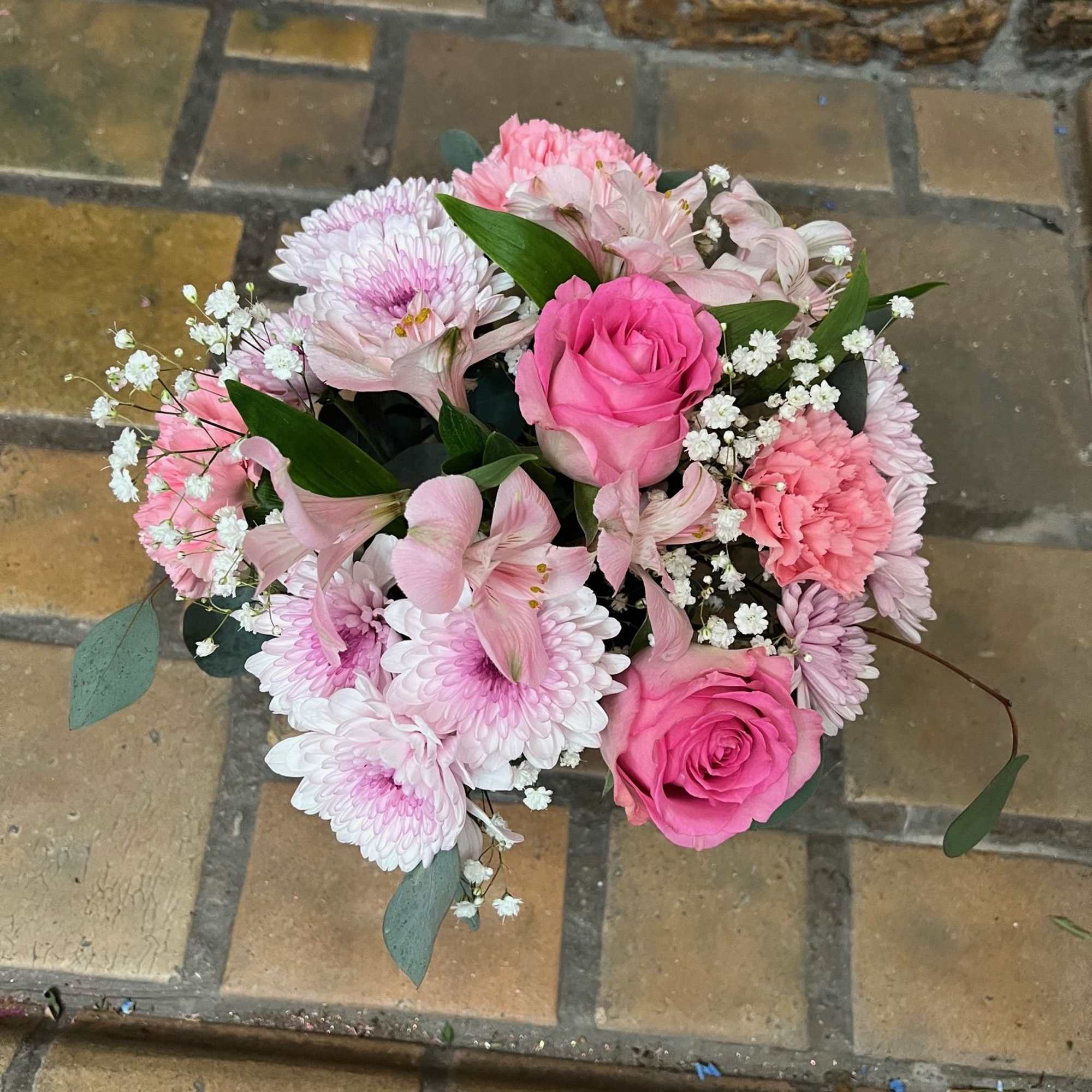 Different shade of pink flowers are arranged inside a clear cylinder vase.


