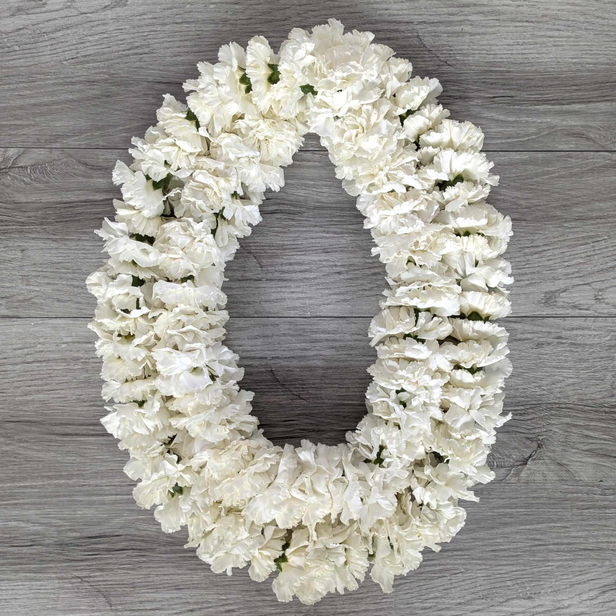 White carnation lei arranged in a U shape on a wood surface