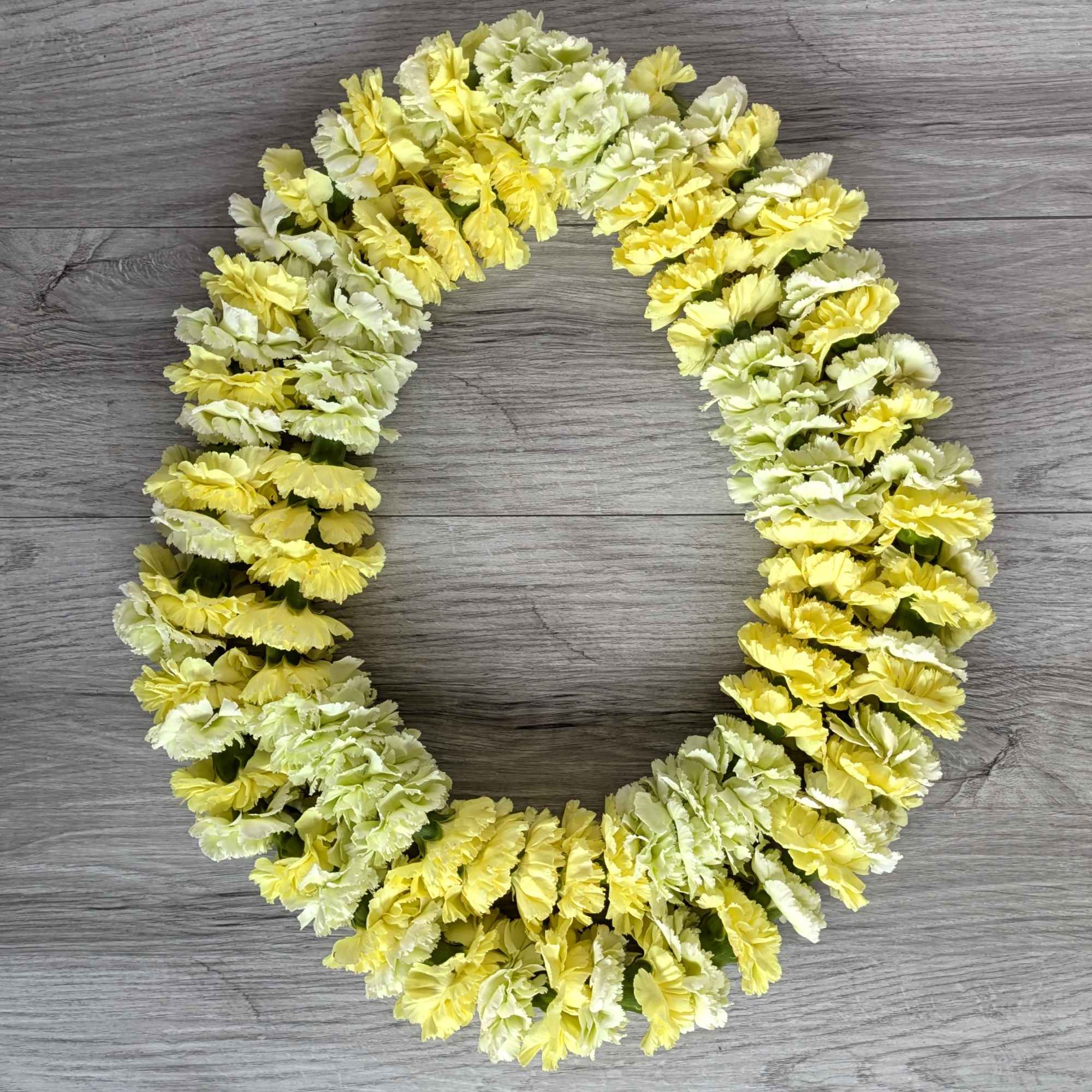 Yellow and white carnation lei arranged in a circle on a wood surface