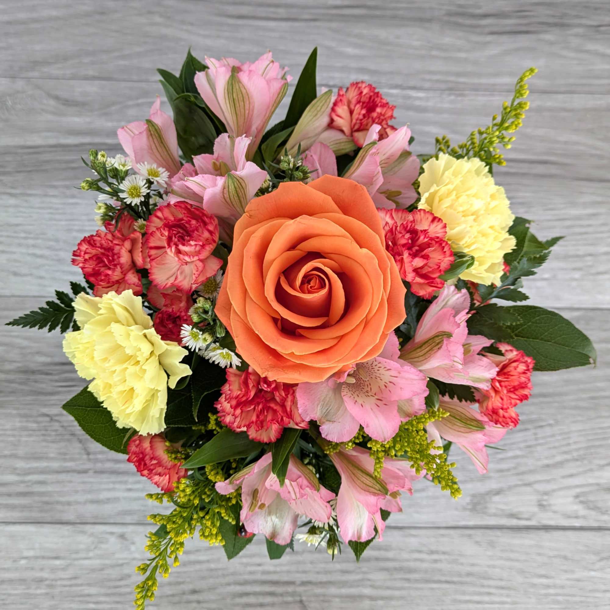 Bouquet with an orange rose, pink flowers, and yellow carnations