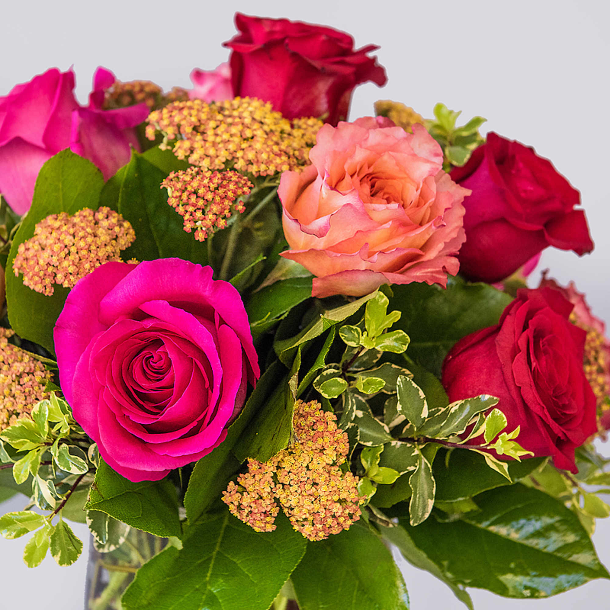 Arrangement of hot pink, red, and peach roses with small yellow clusters in a glass vase
