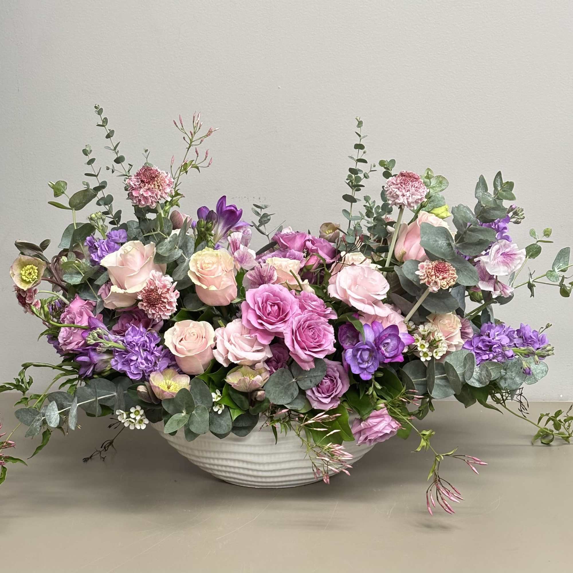 Low pink and purple flower arrangement in a white ceramic bowl