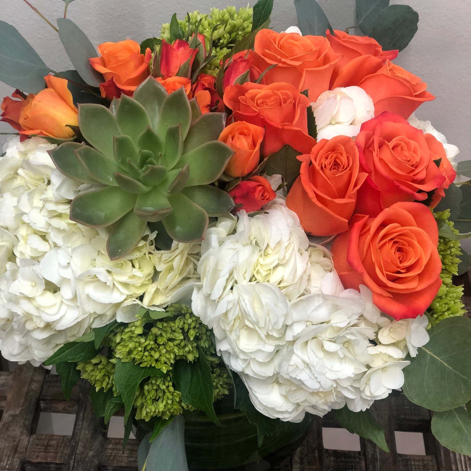 Bouquet of orange roses, white hydrangeas, and a green succulent in a vase