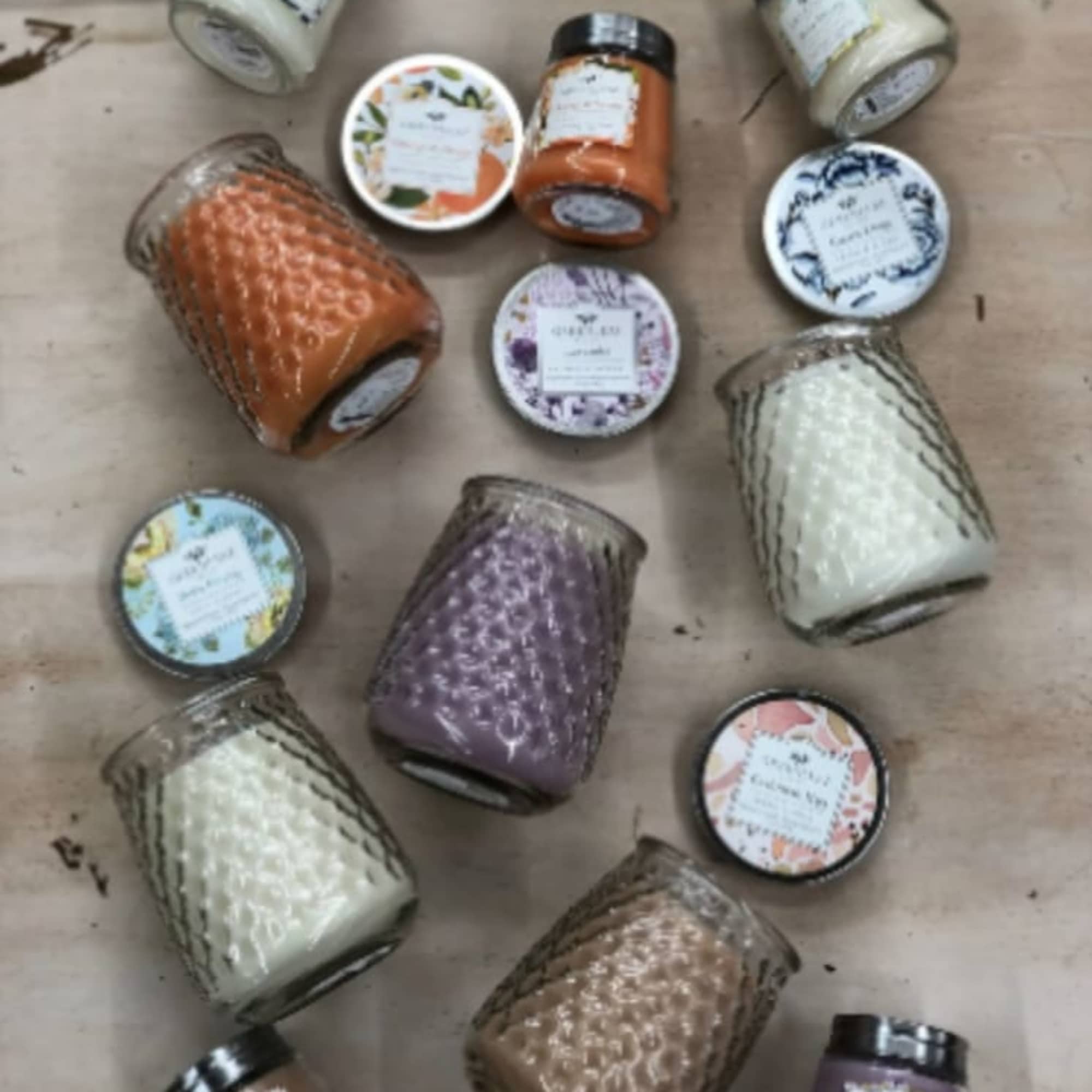 Assorted colored candles in textured glass jars with decorative lids arranged on a wooden surface