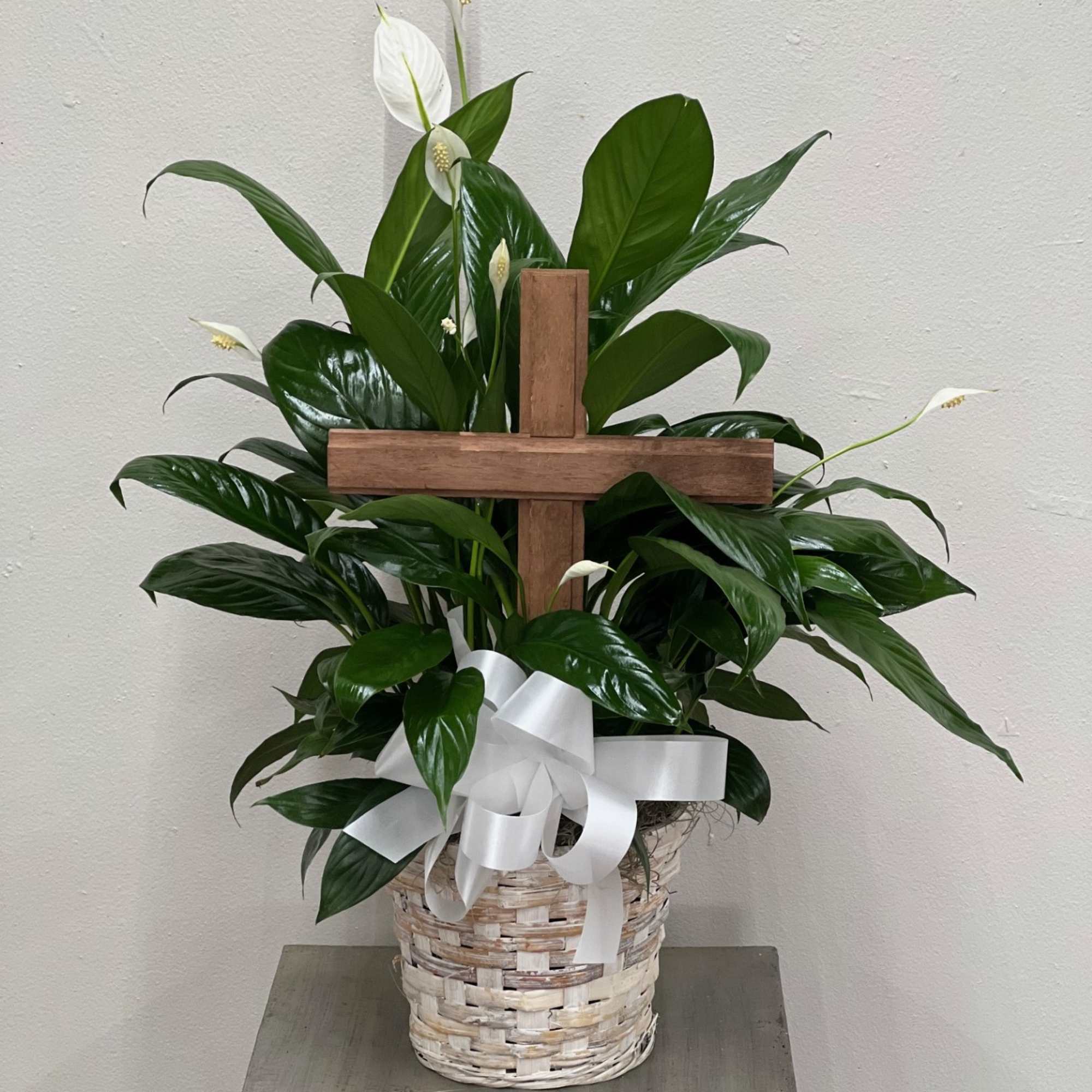 White peace lilies in a wicker basket with a wooden cross and white ribbon