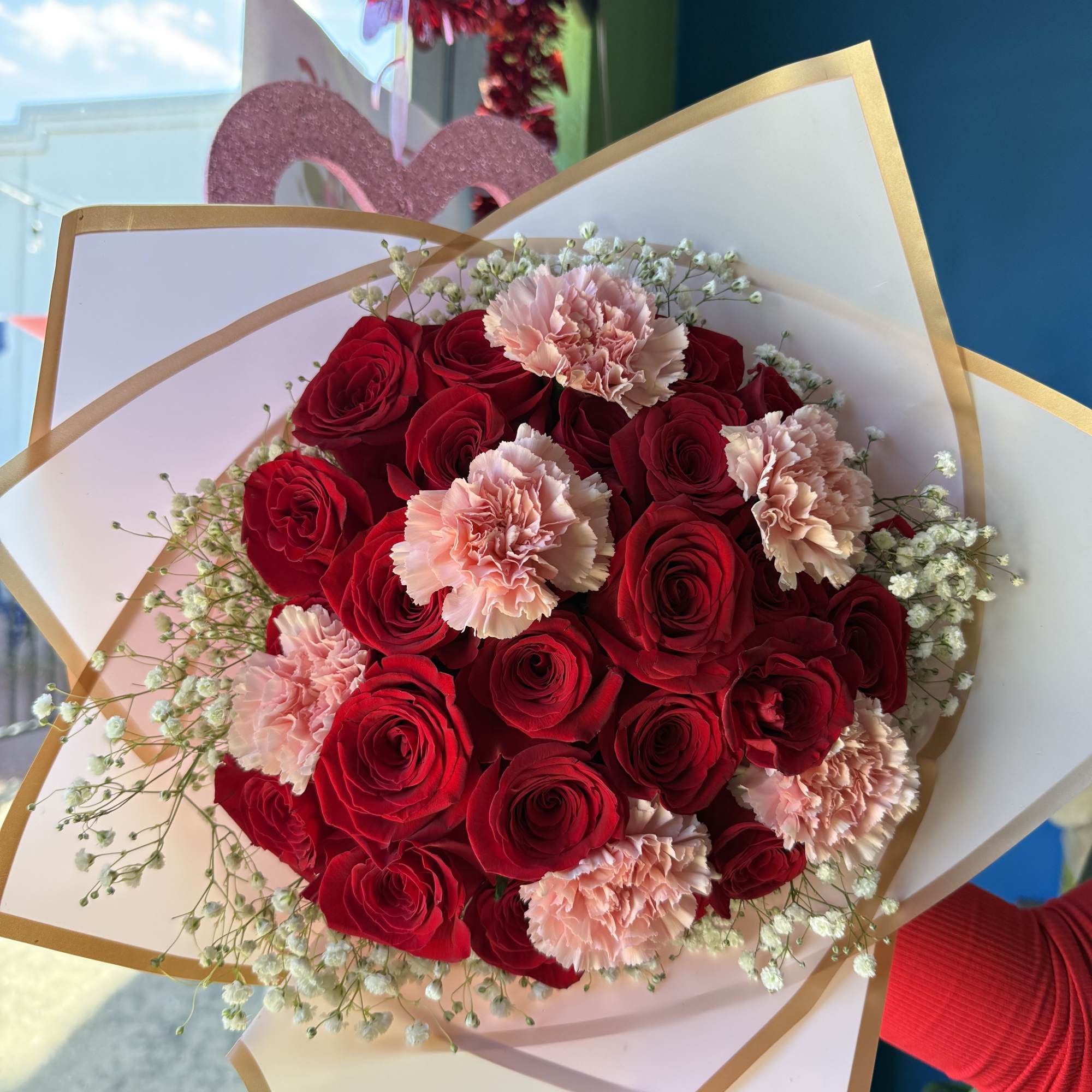 Bouquet of red roses and pale pink carnations wrapped in white paper