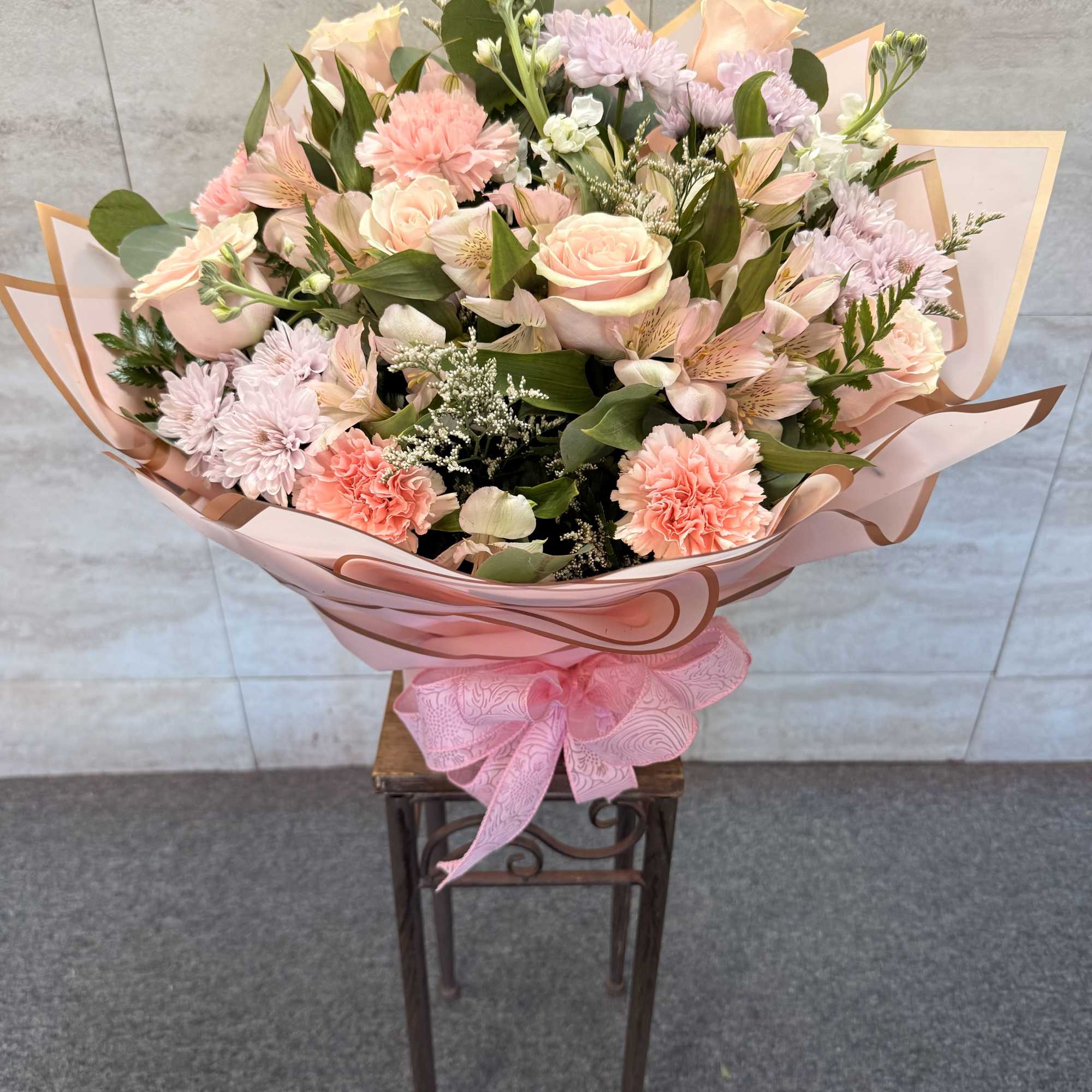 Large bouquet of pink and peach flowers wrapped in pink paper with a ribbon