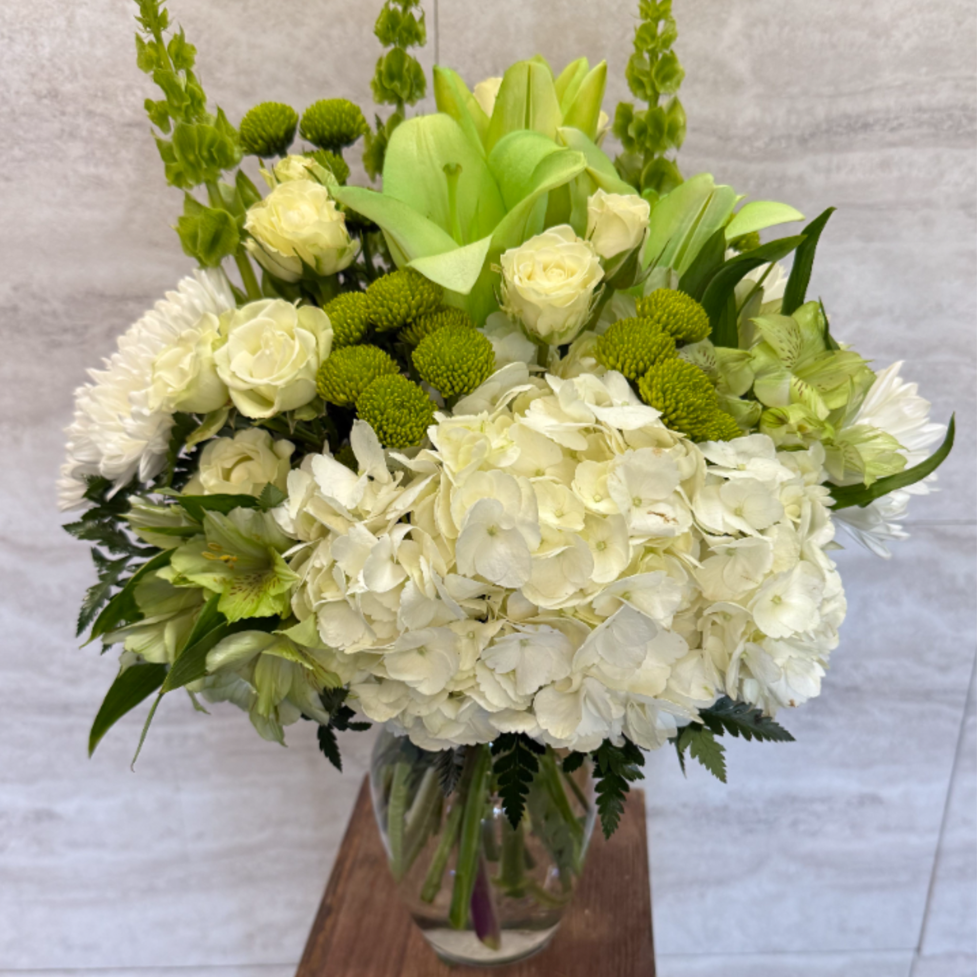 Tall white and green flower arrangement with hydrangeas and roses in a clear glass vase