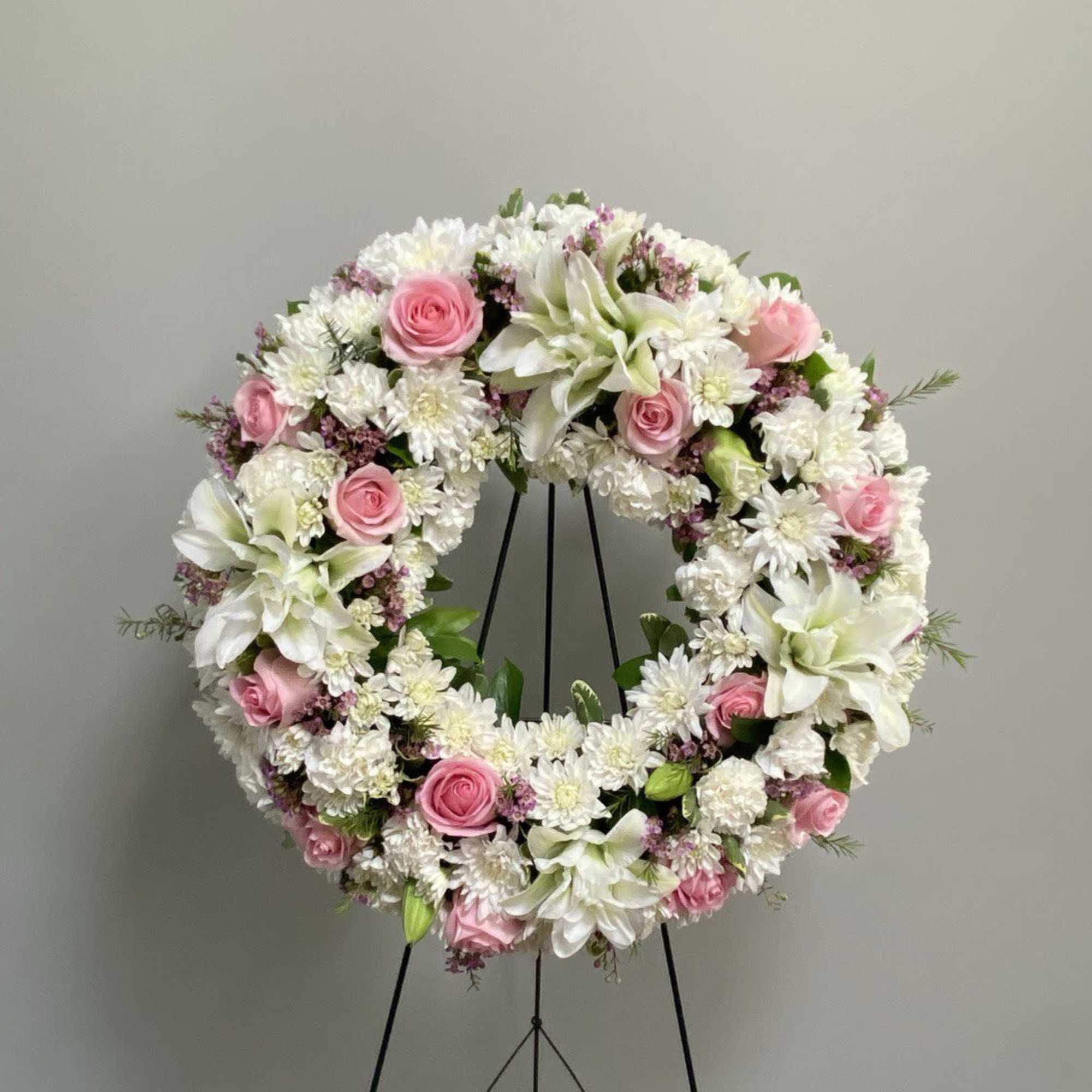 Circular floral wreath with pink roses and white blooms on a black stand