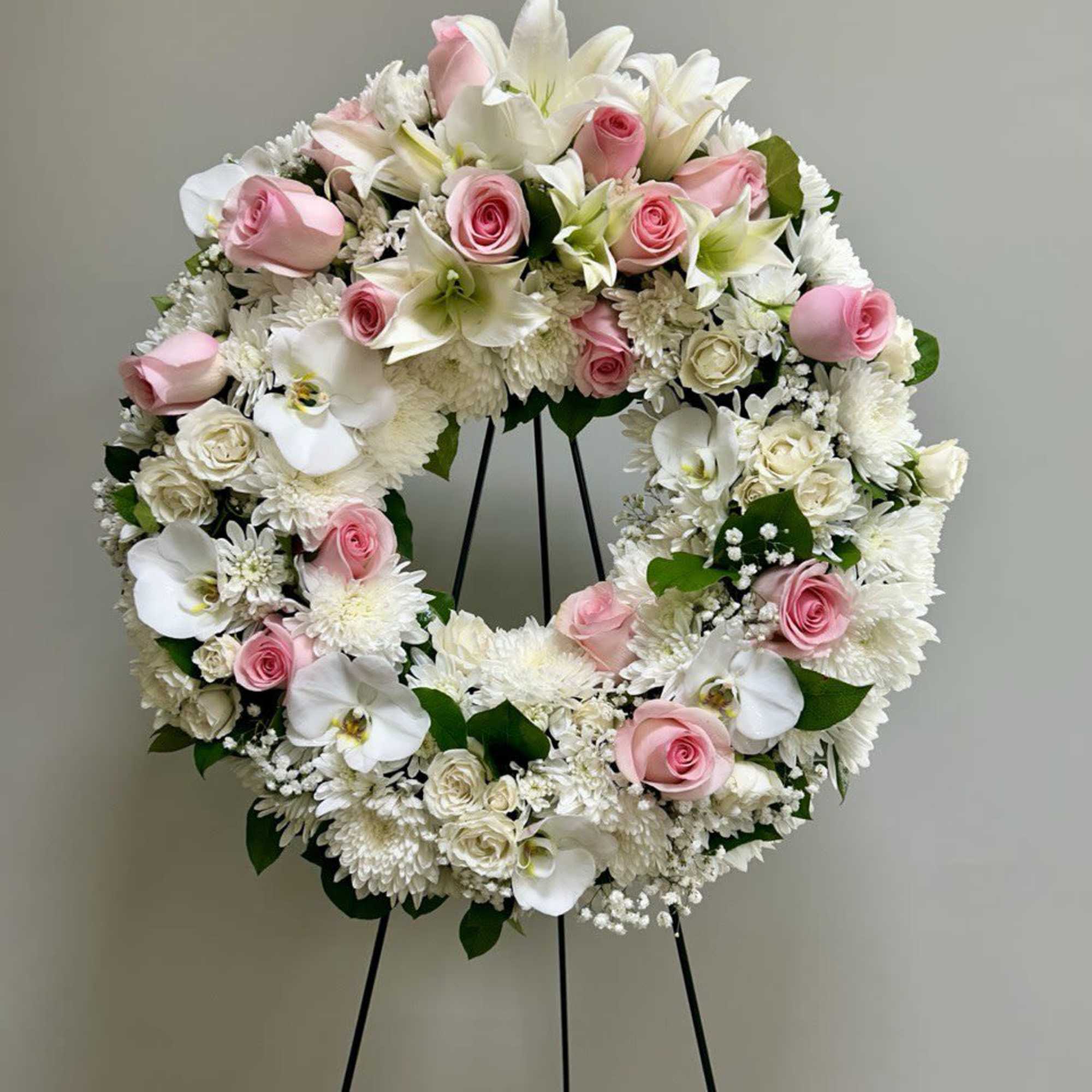 Pink and white floral wreath on a black stand