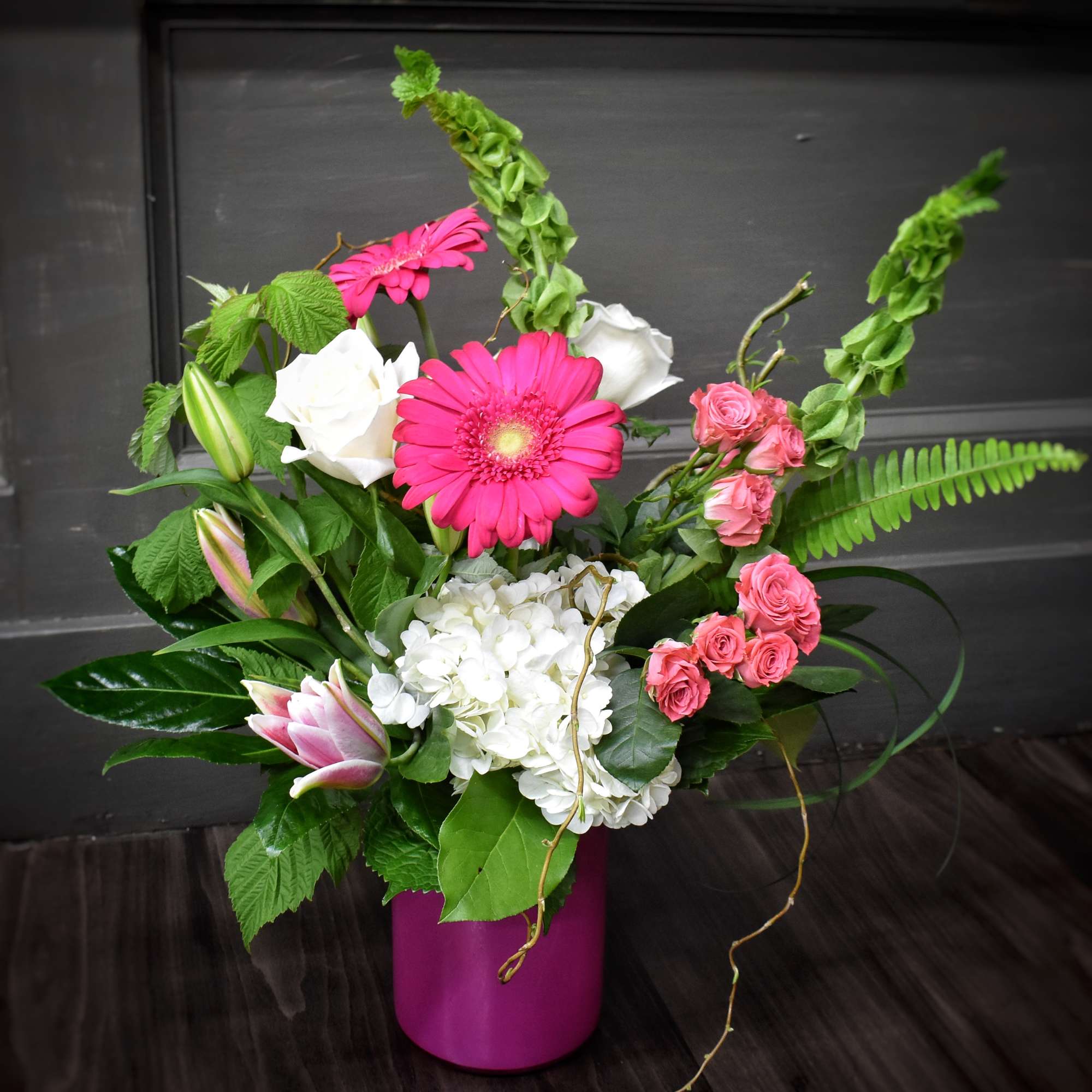 Pink gerbera and roses with white hydrangea in a magenta vase