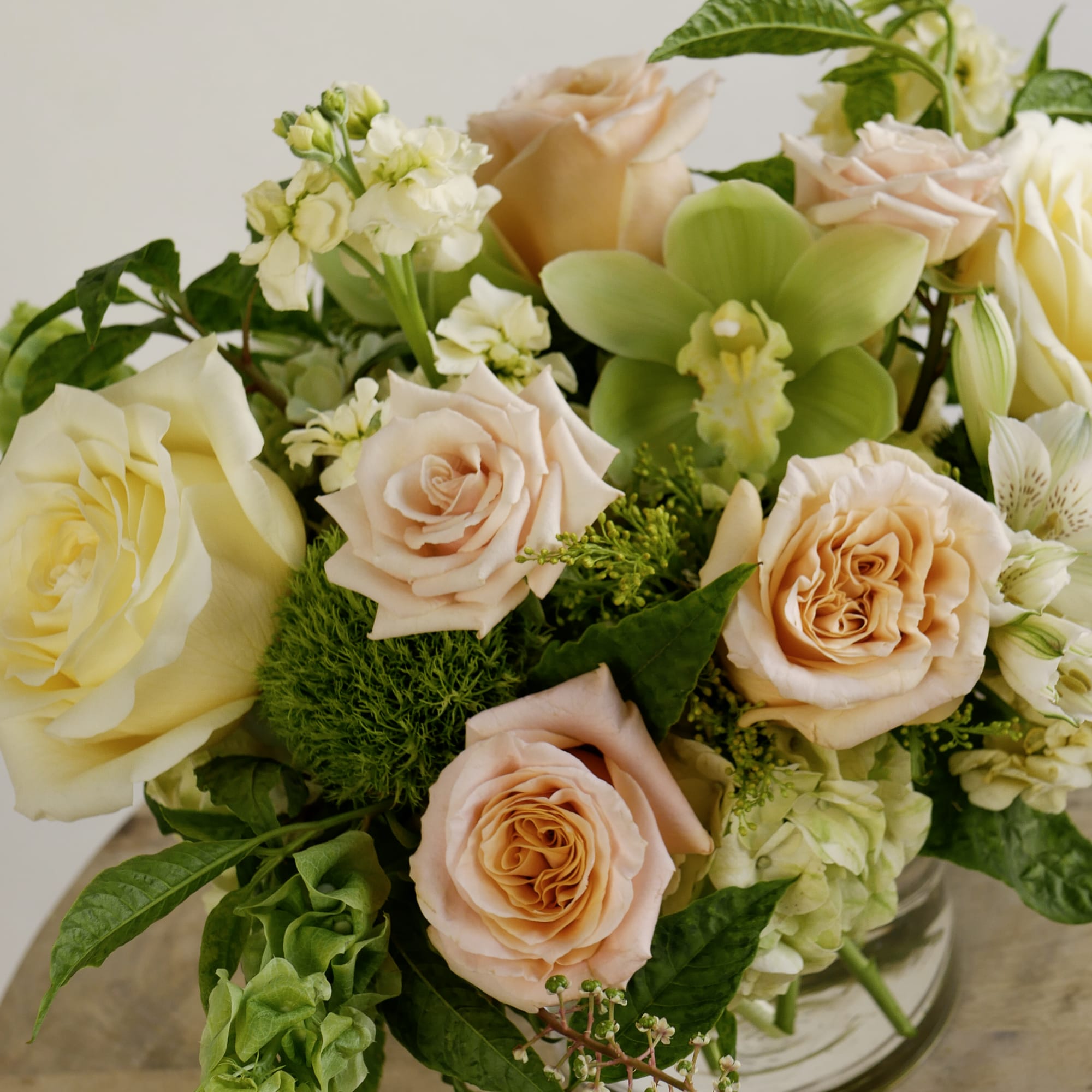 Bouquet of peach and cream roses with green orchids in a glass vase