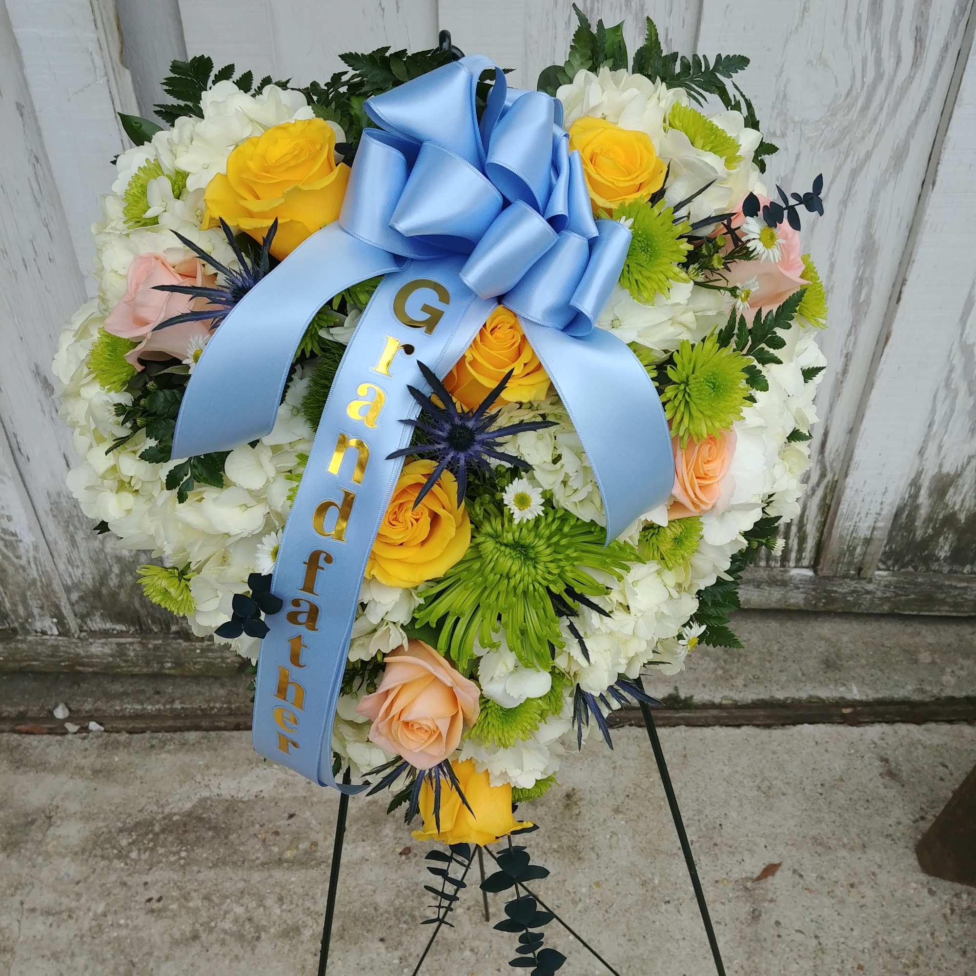 Heart-shaped floral wreath with a blue ribbon and yellow roses