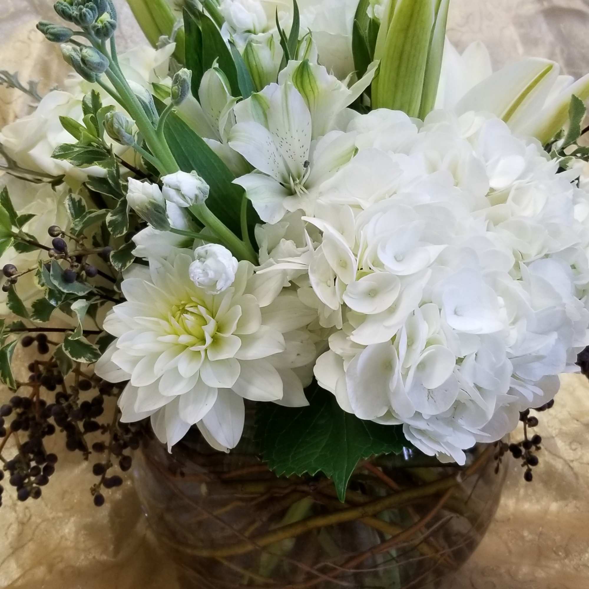 White floral arrangement in a glass vase with lilies and hydrangeas