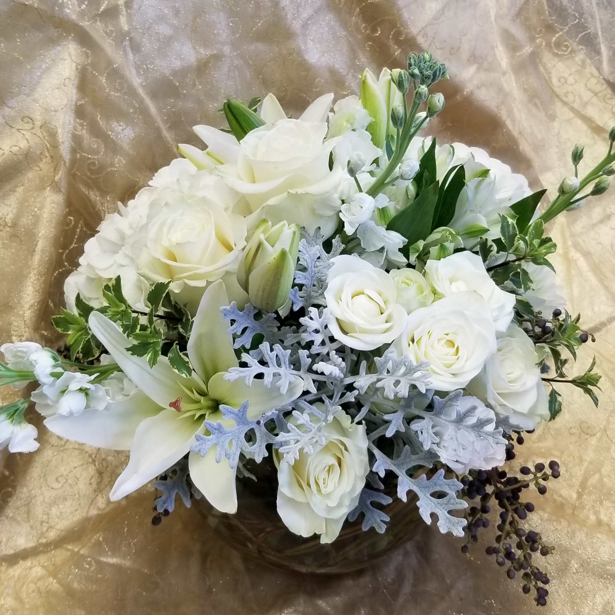 White rose and lily bouquet with silver foliage on gold fabric