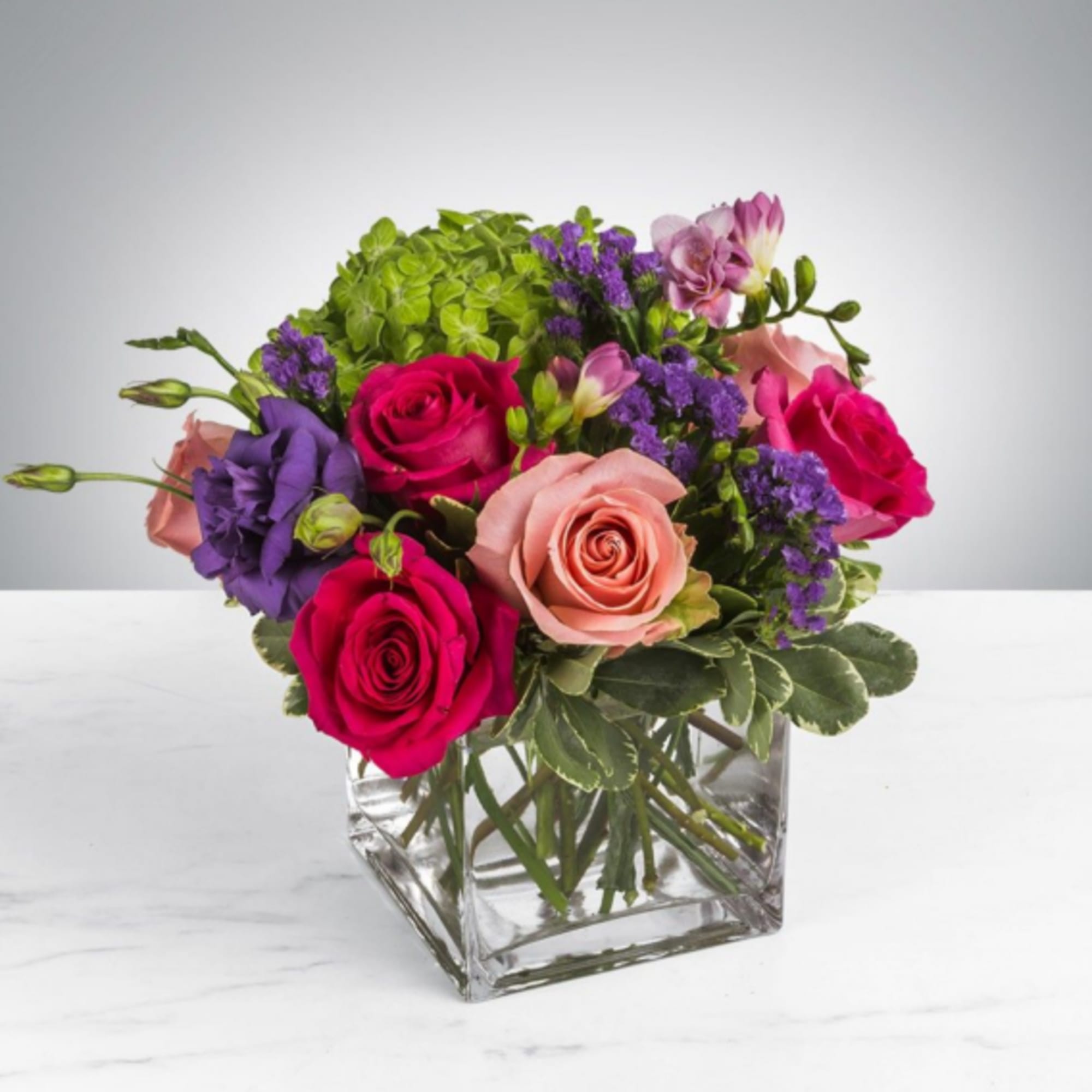 This arrangement includes hot pink roses, pink roses, green hydrangea, freesia, lisianthus