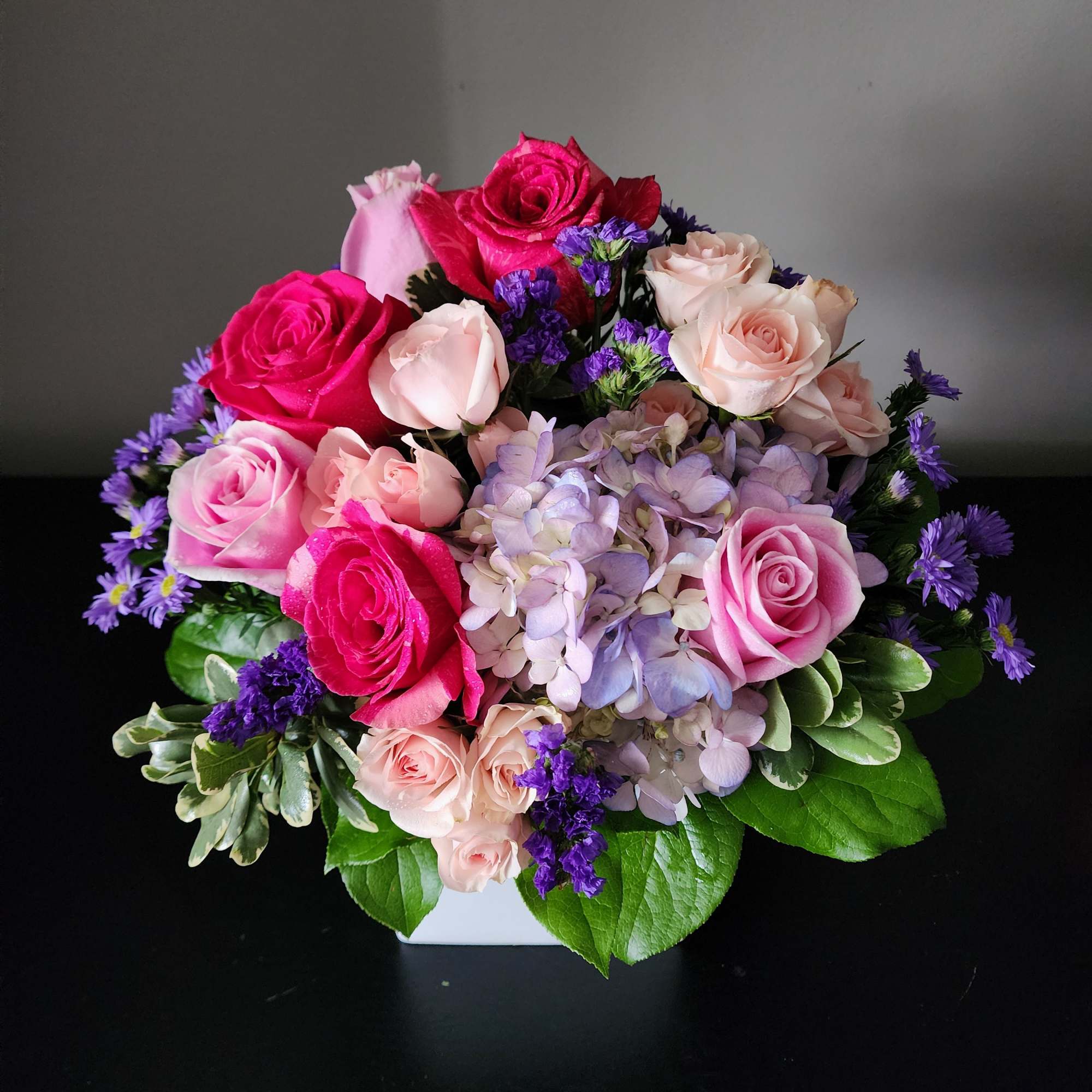 Pink and lavender rose bouquet in a white container