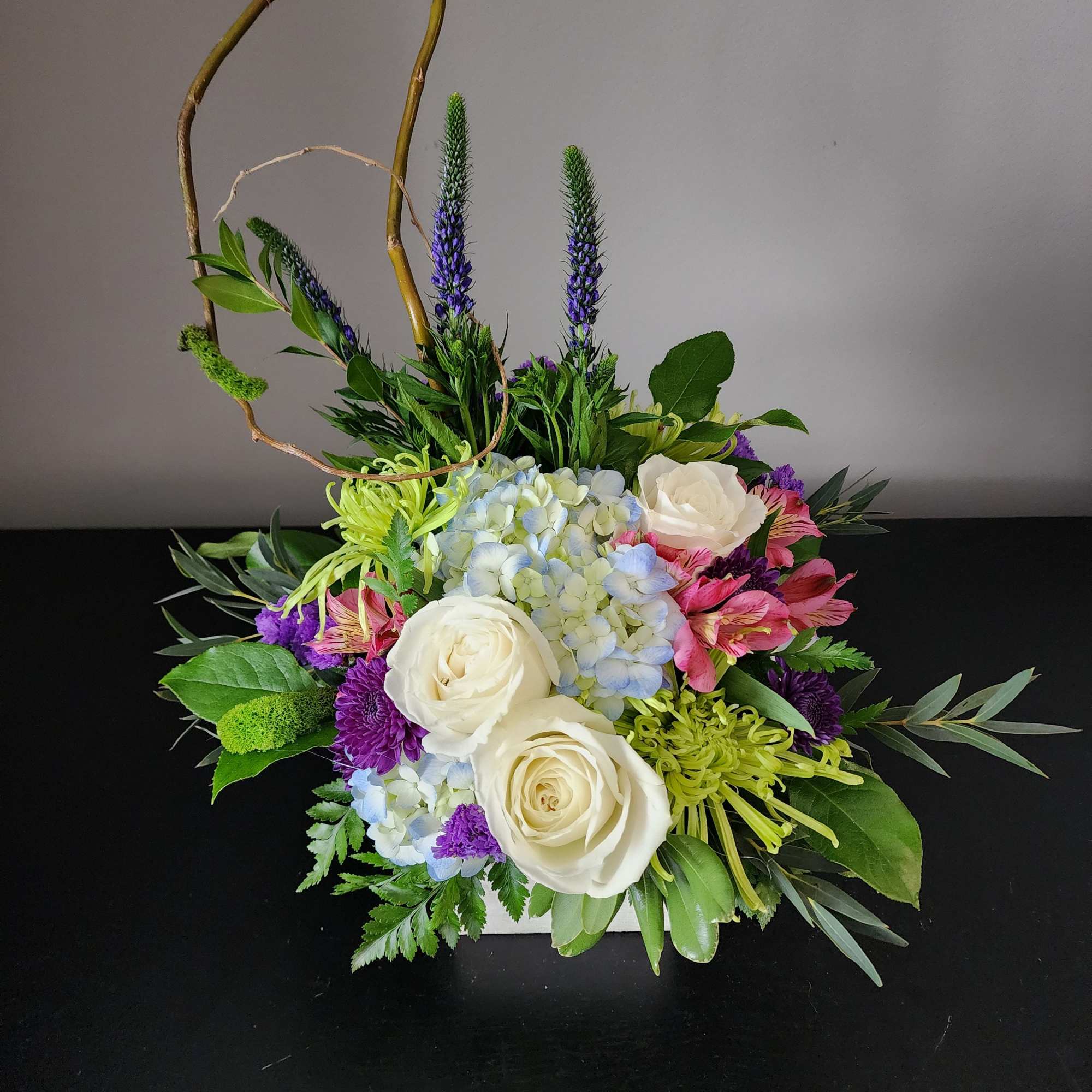 Mixed floral arrangement with white roses, blue hydrangea, and purple accents