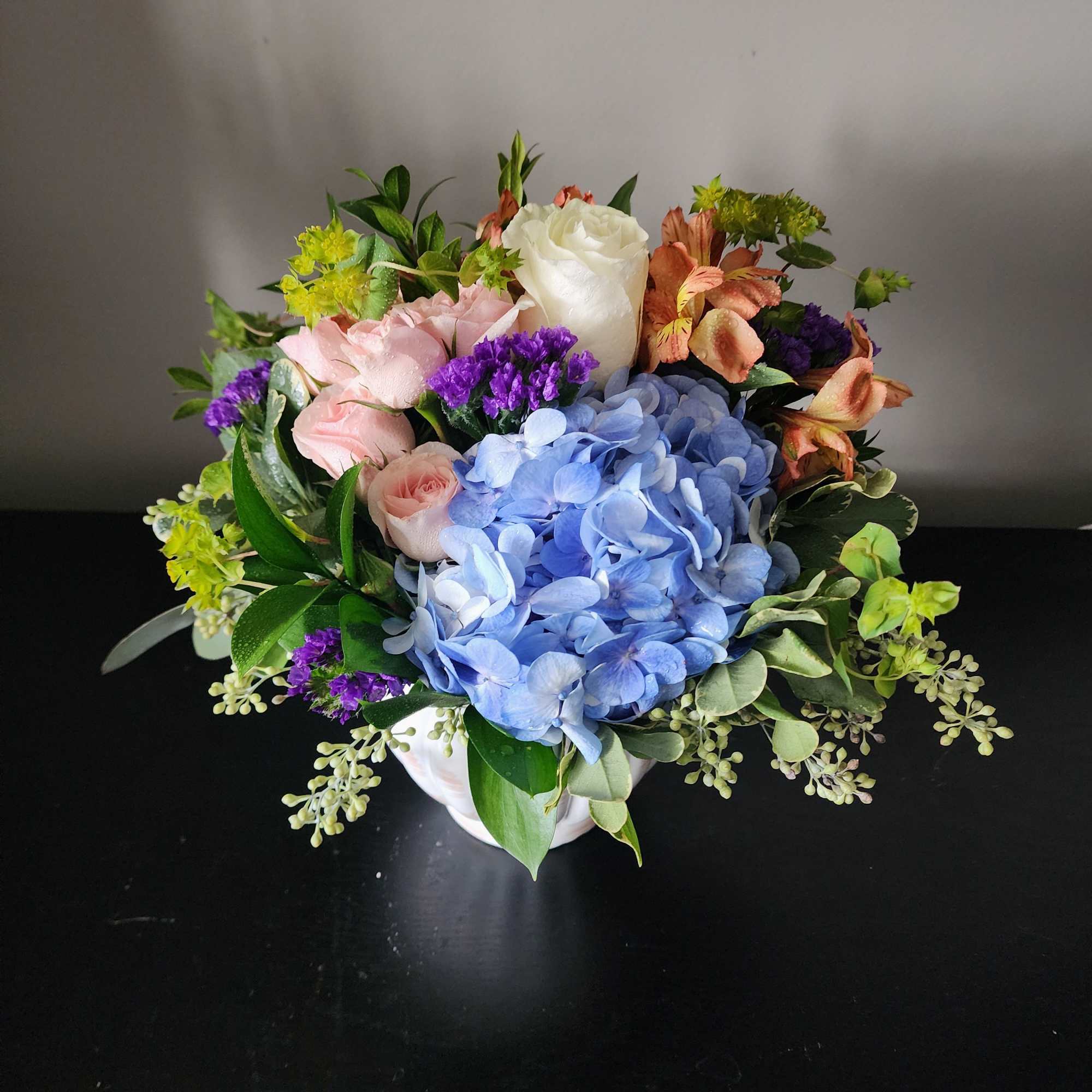 Mixed bouquet with blue hydrangea, pink roses, and white rose in a white vase