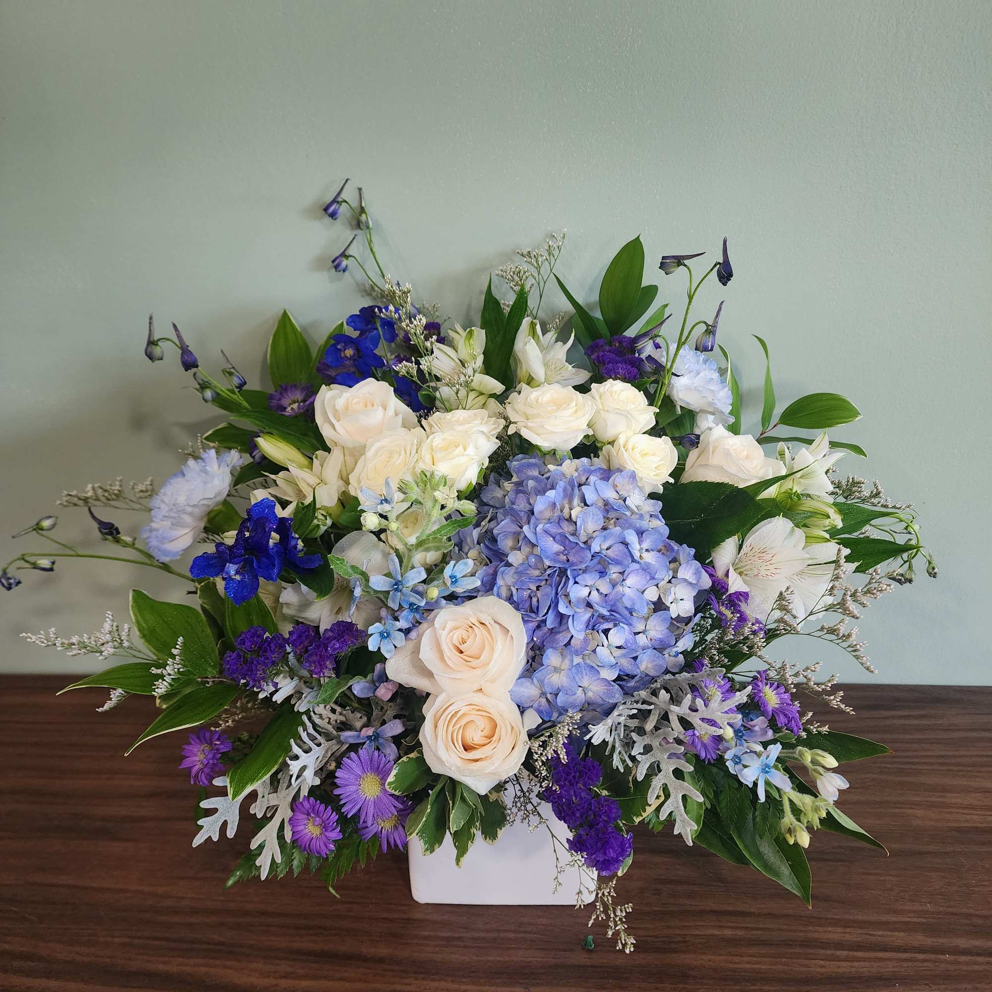 Mixed bouquet of white, blue, and purple flowers in a white container