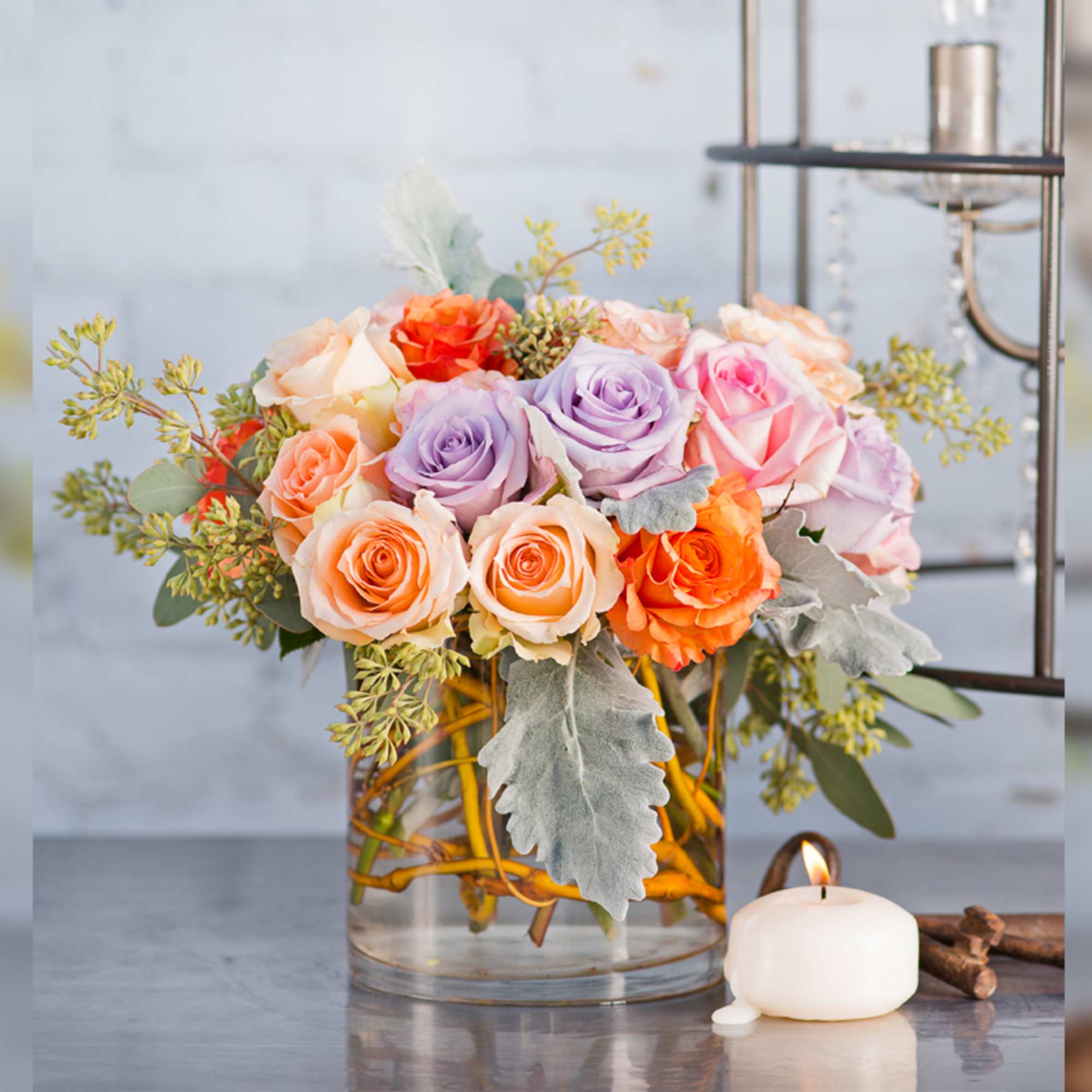 Mixed roses in a clear glass vase beside a lit candle