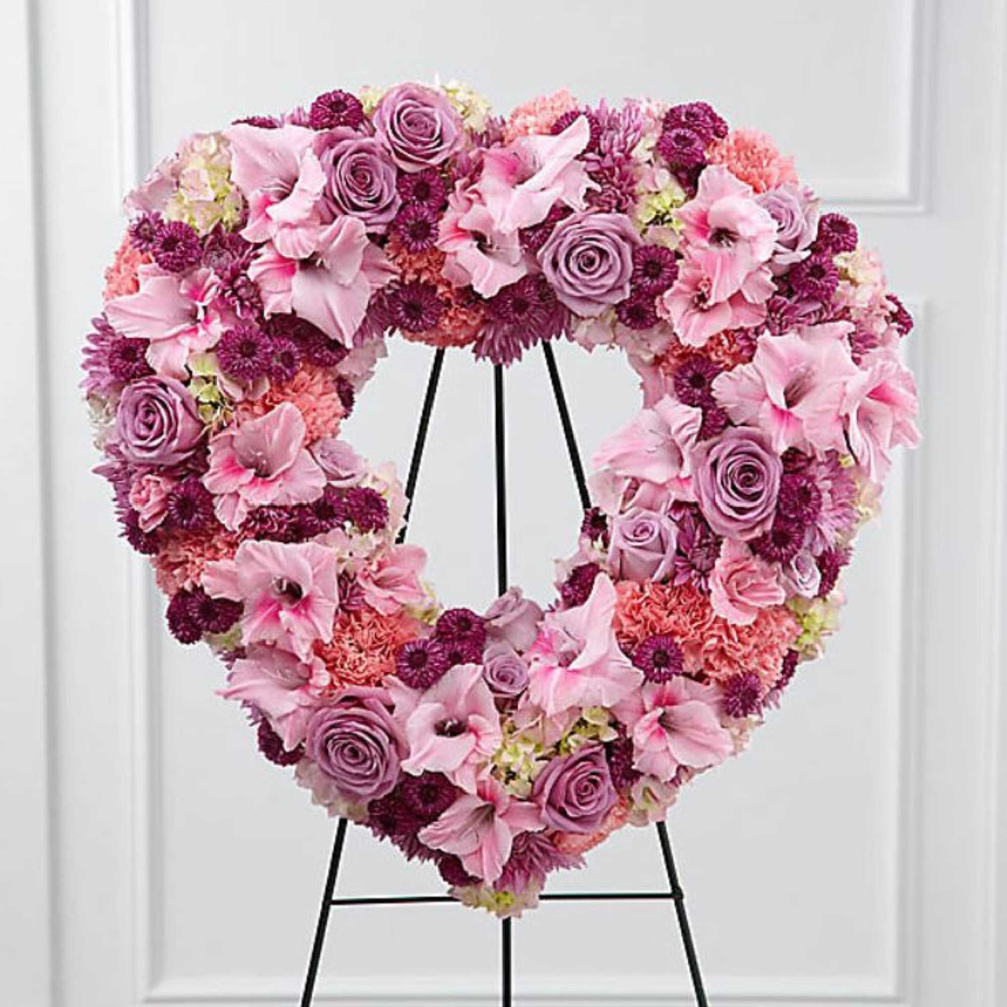 Heart-shaped floral wreath in pink and purple tones on a black stand