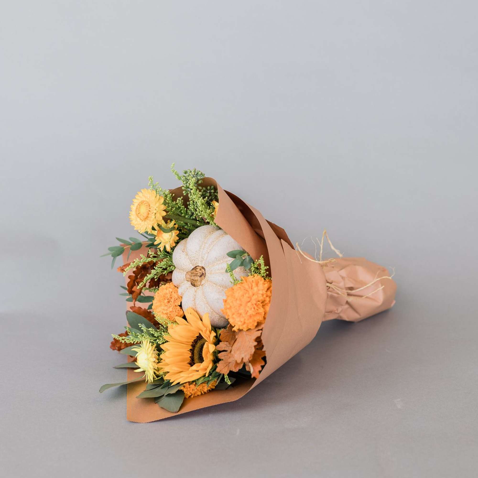 Bouquet with a white pumpkin and orange-yellow flowers wrapped in brown paper