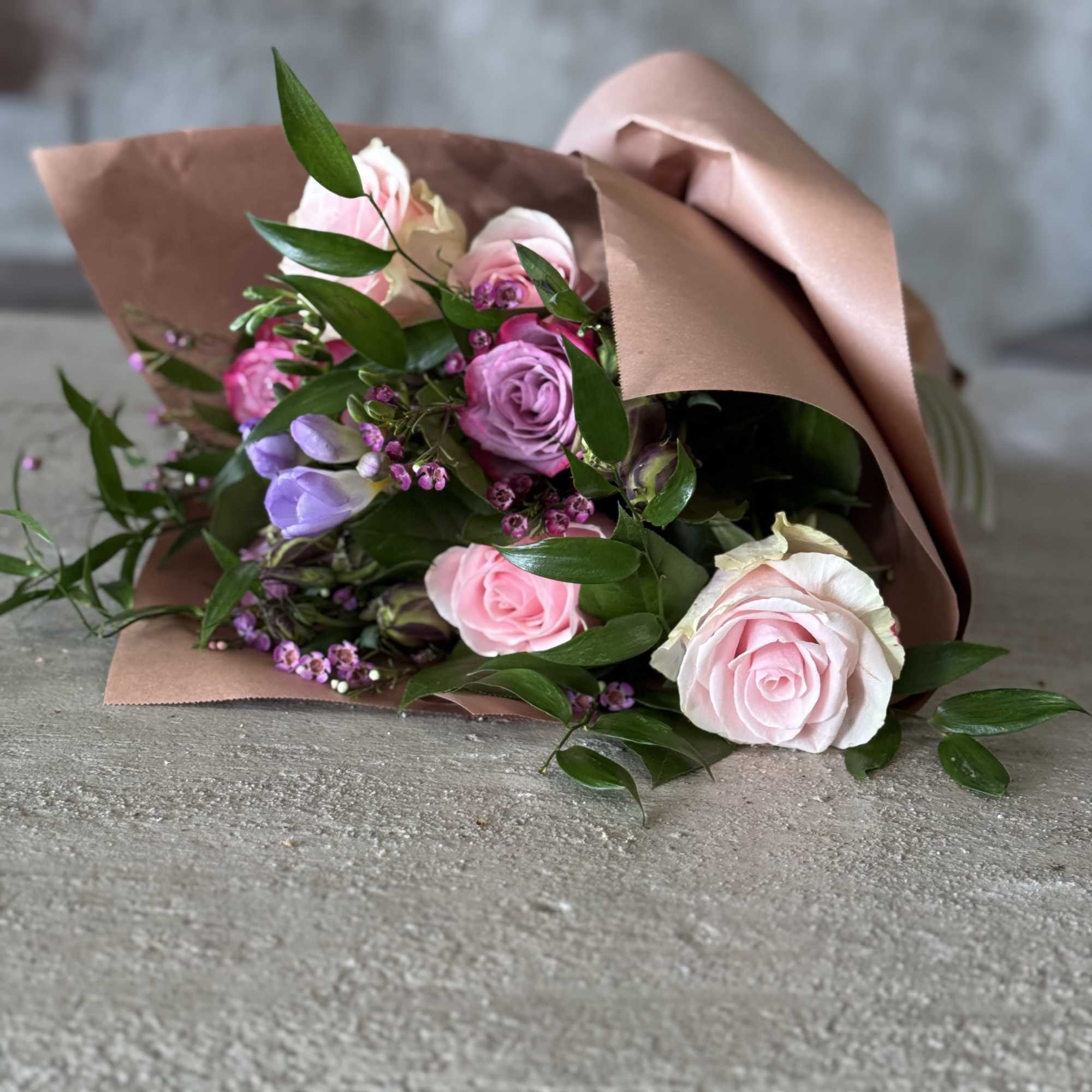 Bouquet of pink and lavender roses wrapped in brown paper