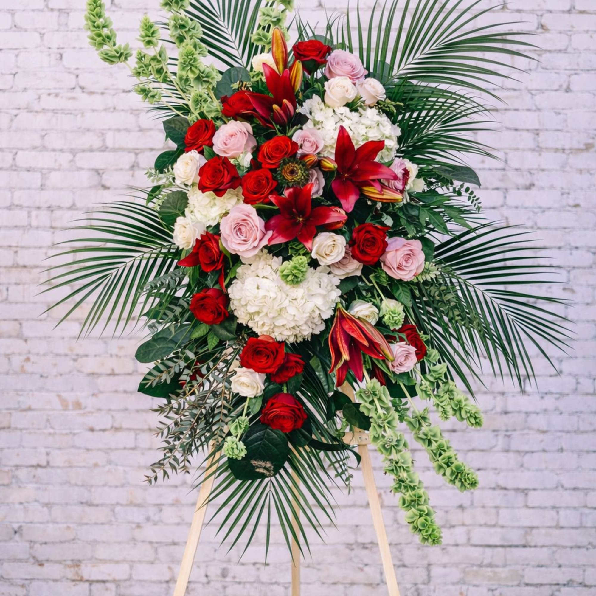 Standing floral spray with red and pink roses and lilies on an easel
