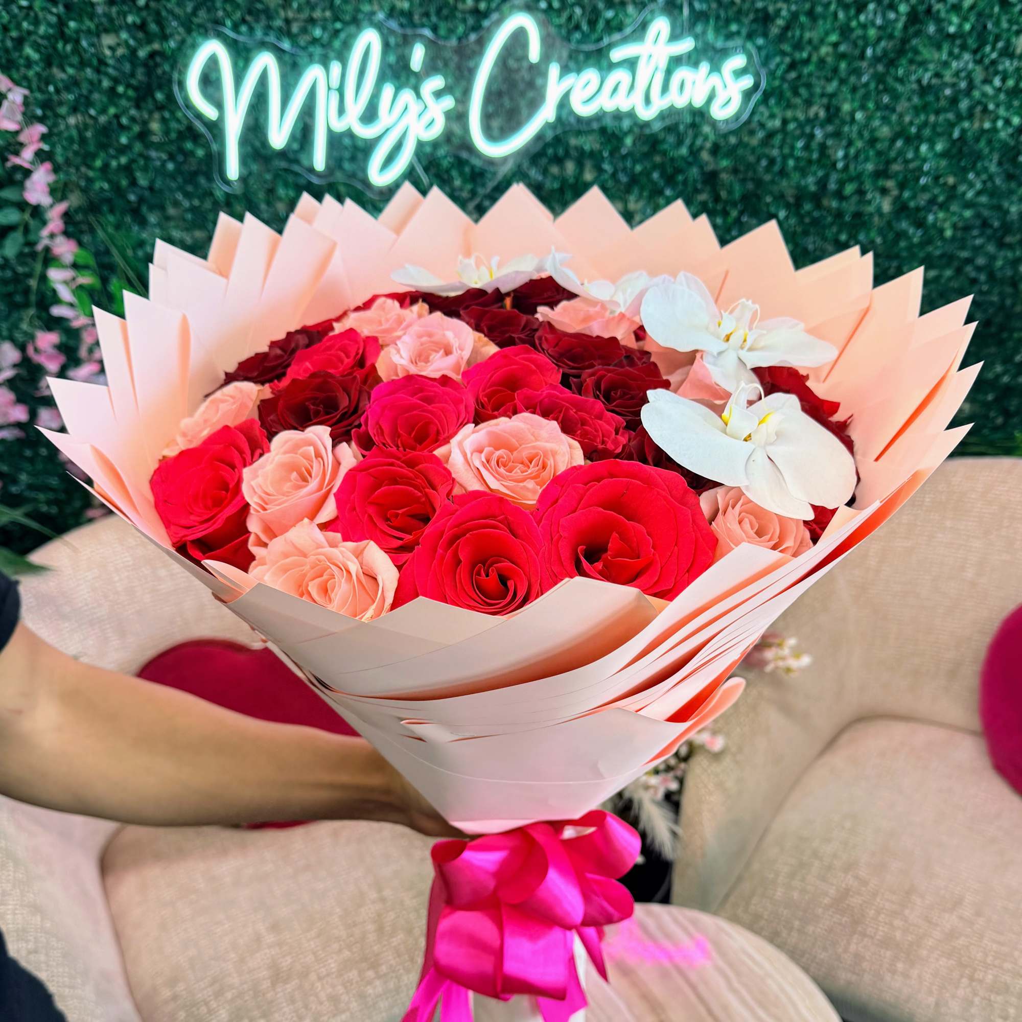 Bouquet of red, pink, and peach roses with white orchids in pale wrapping