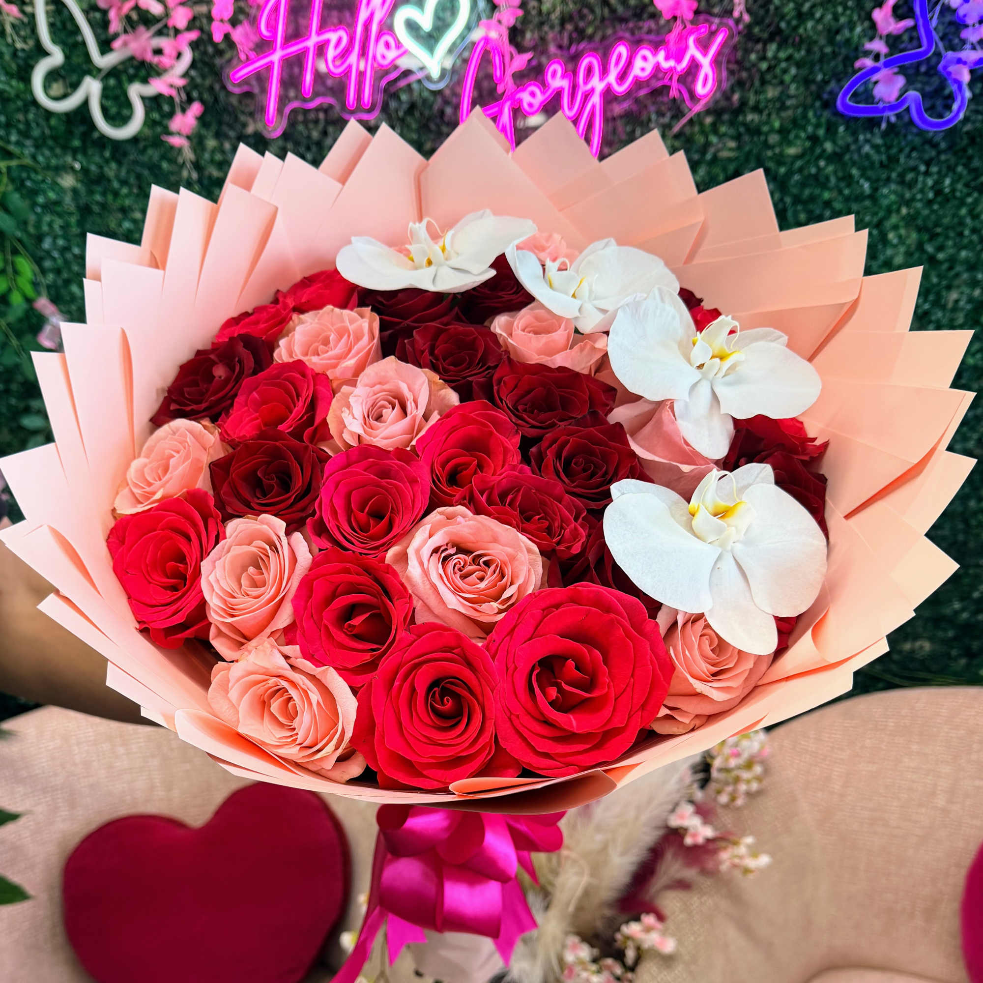 Bouquet of red and pink roses with white orchids in peach wrapping