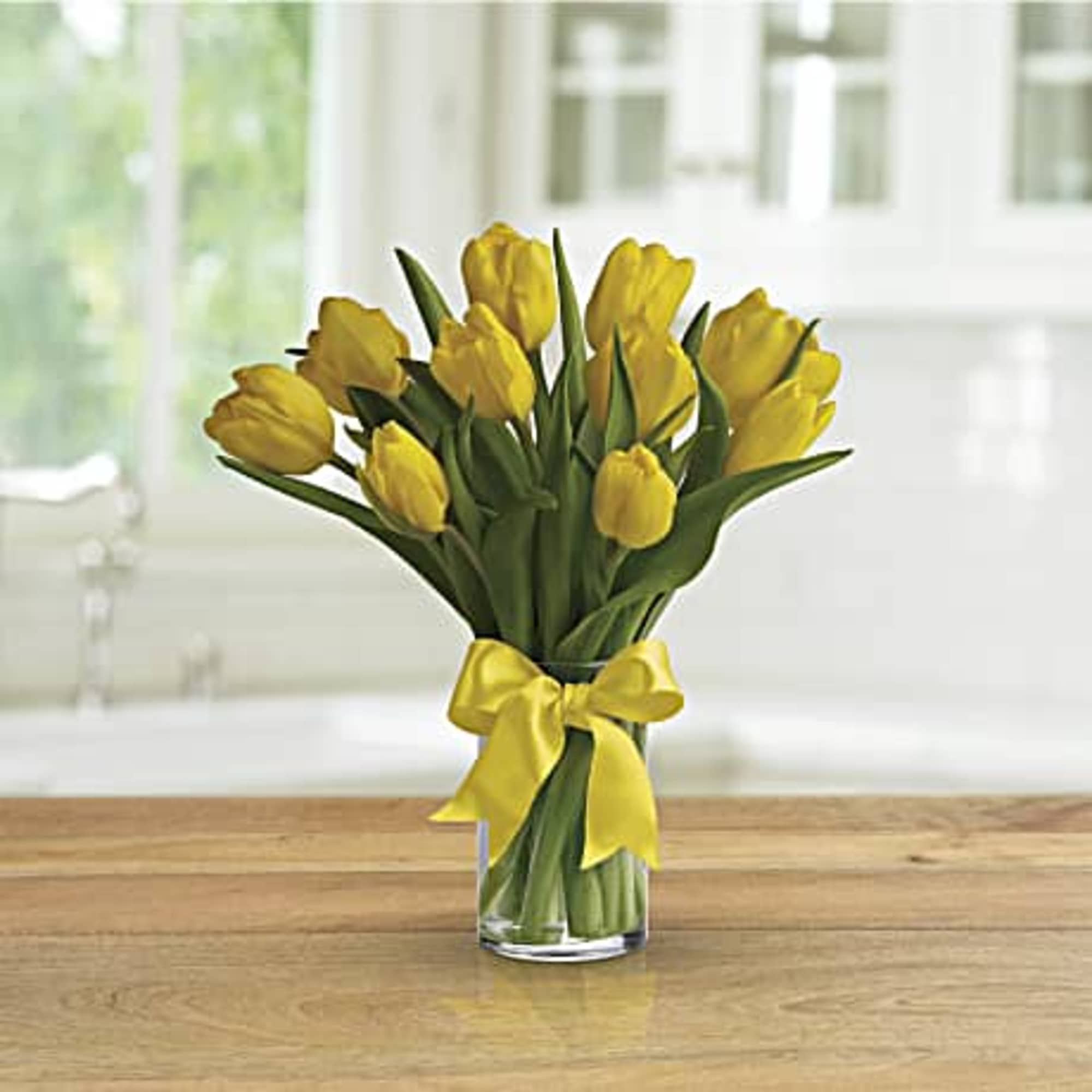 Yellow tulips in a clear glass vase tied with a yellow ribbon.