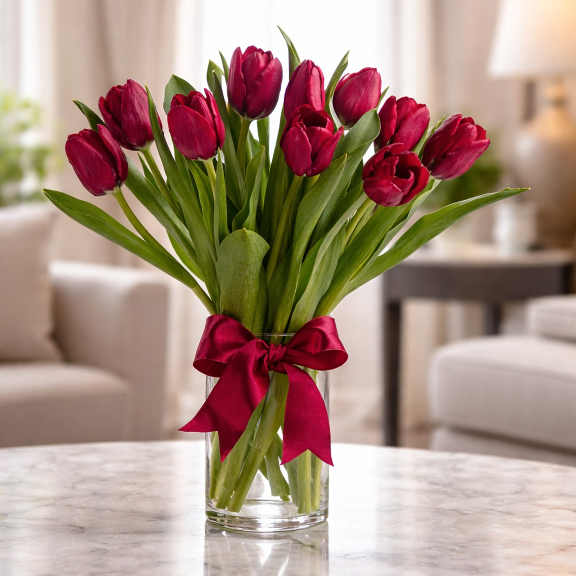 Red tulips in a clear glass vase with a burgundy ribbon