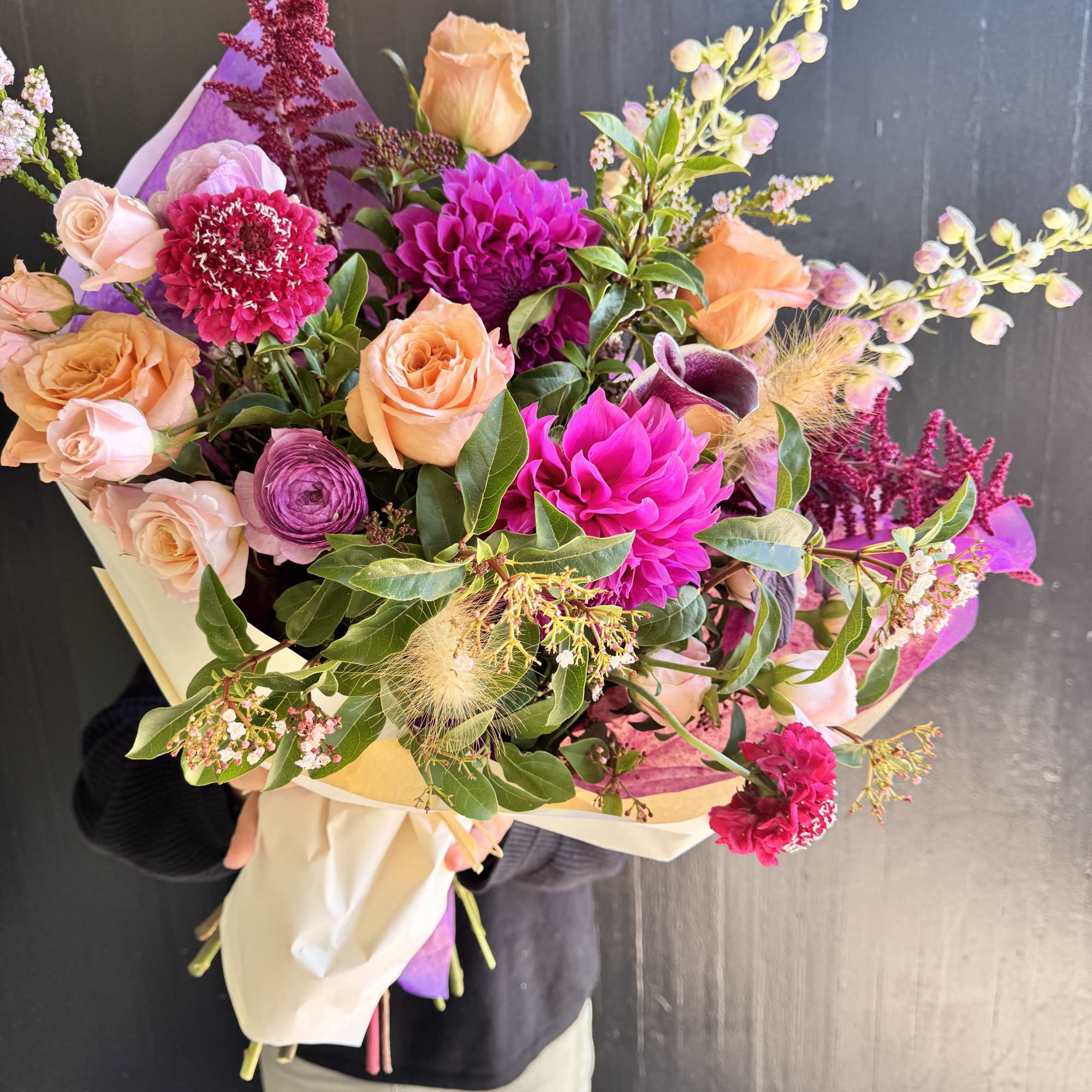 Hand-tied bouquet of peach and magenta flowers wrapped in paper