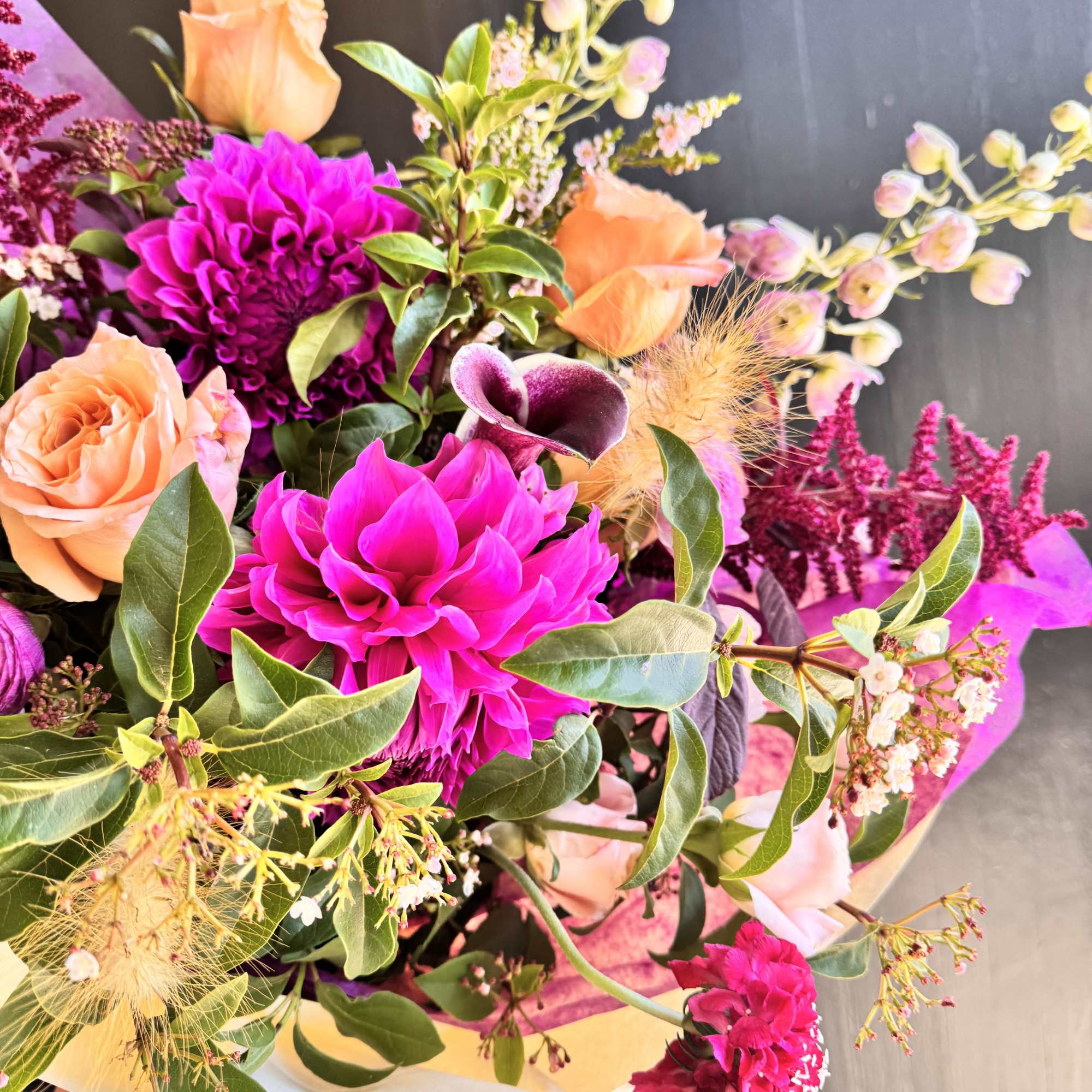 Bouquet of peach roses, magenta blooms, and purple calla lilies