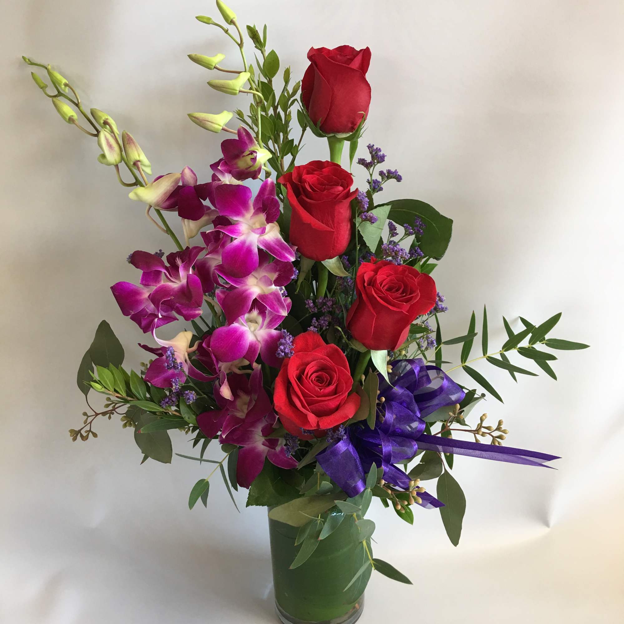Red roses and purple orchids in a glass vase with a ribbon