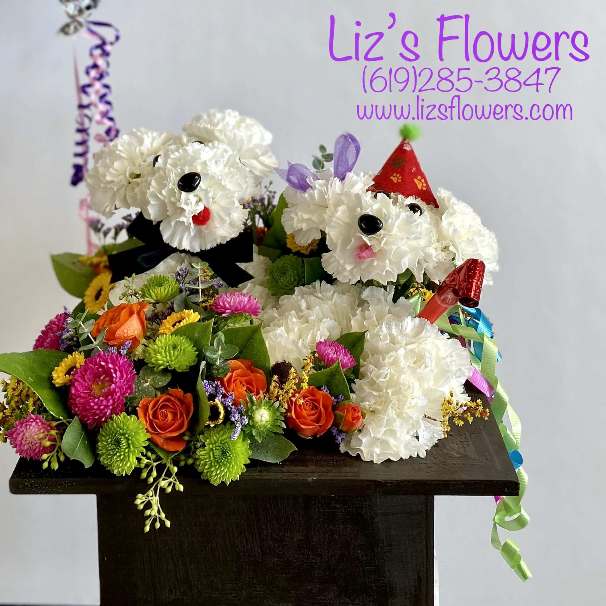 Two floral dog arrangements with party hats and ribbons on a dark pedestal