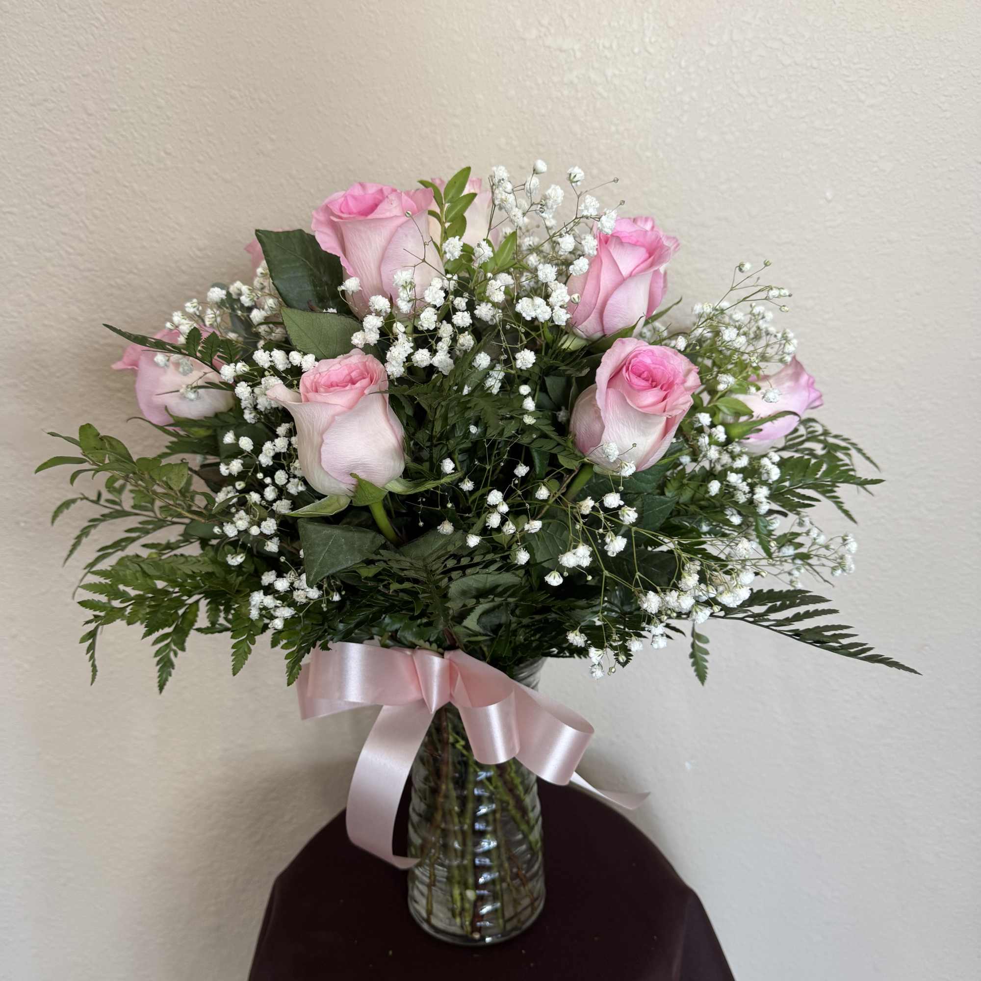 Pink roses and baby's breath in a glass vase with a pink ribbon