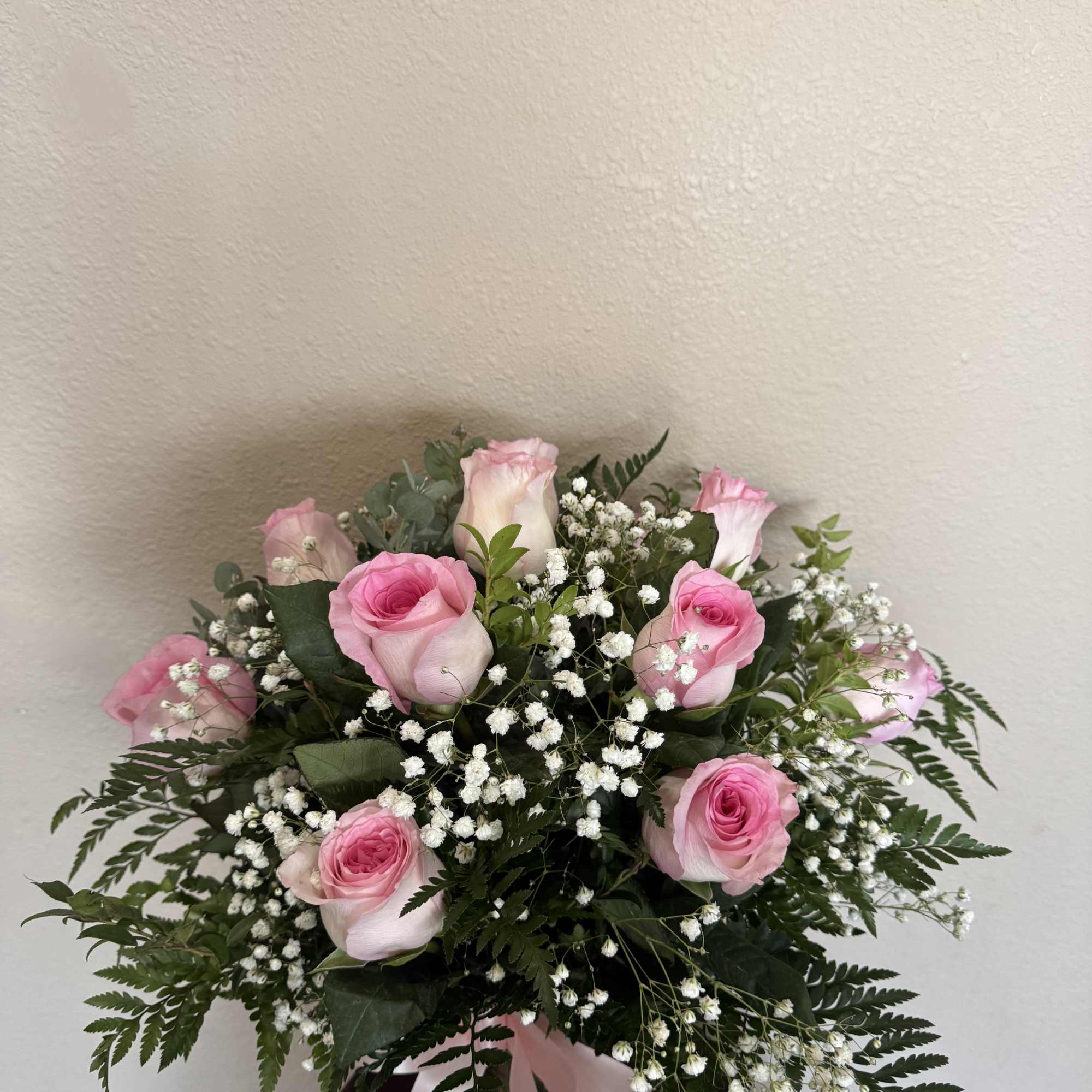 Pink roses with baby's breath in a glass vase with a pink ribbon